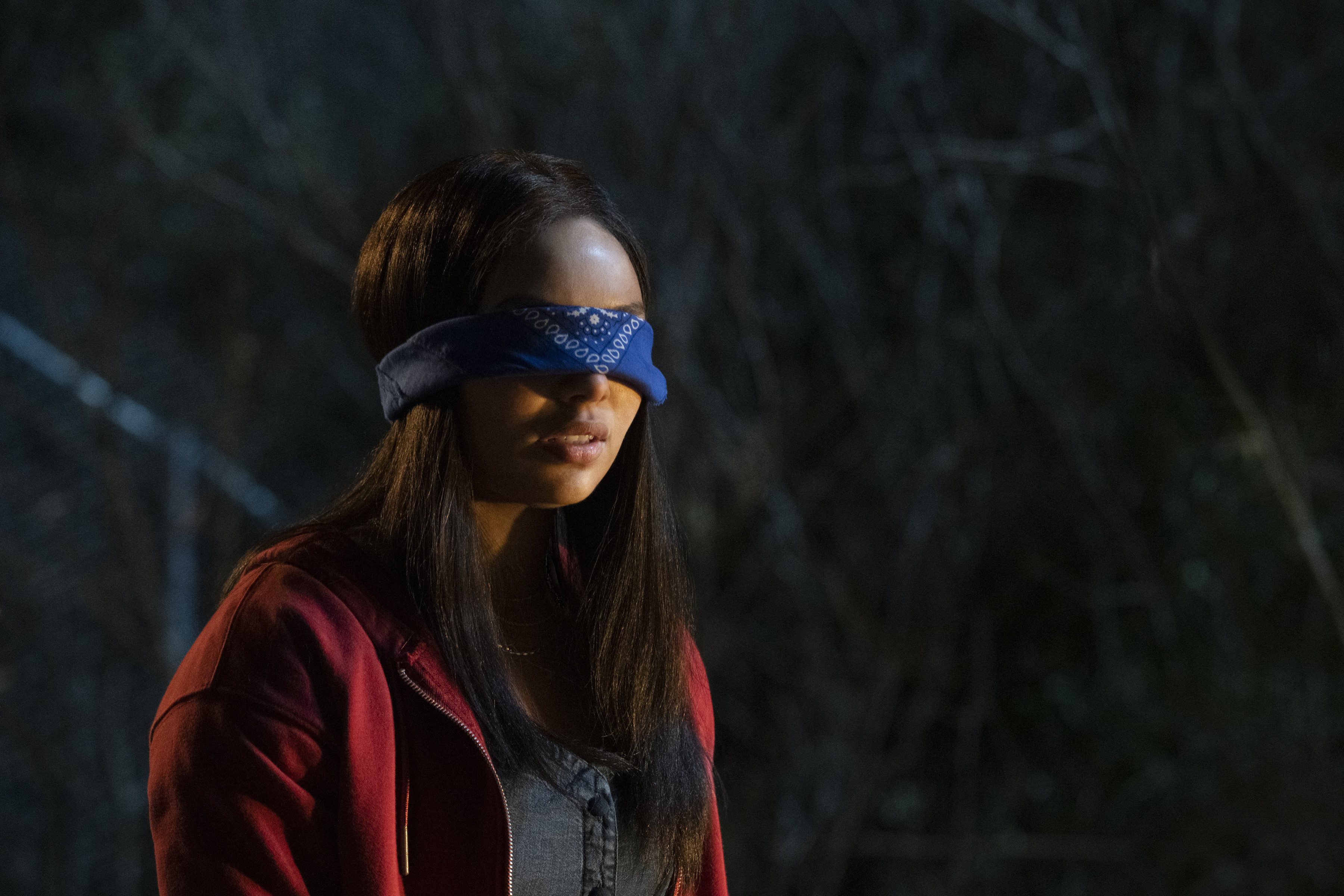 A long-haired teenage girl in a red jacket and bright blue bandana blindfold in Panic