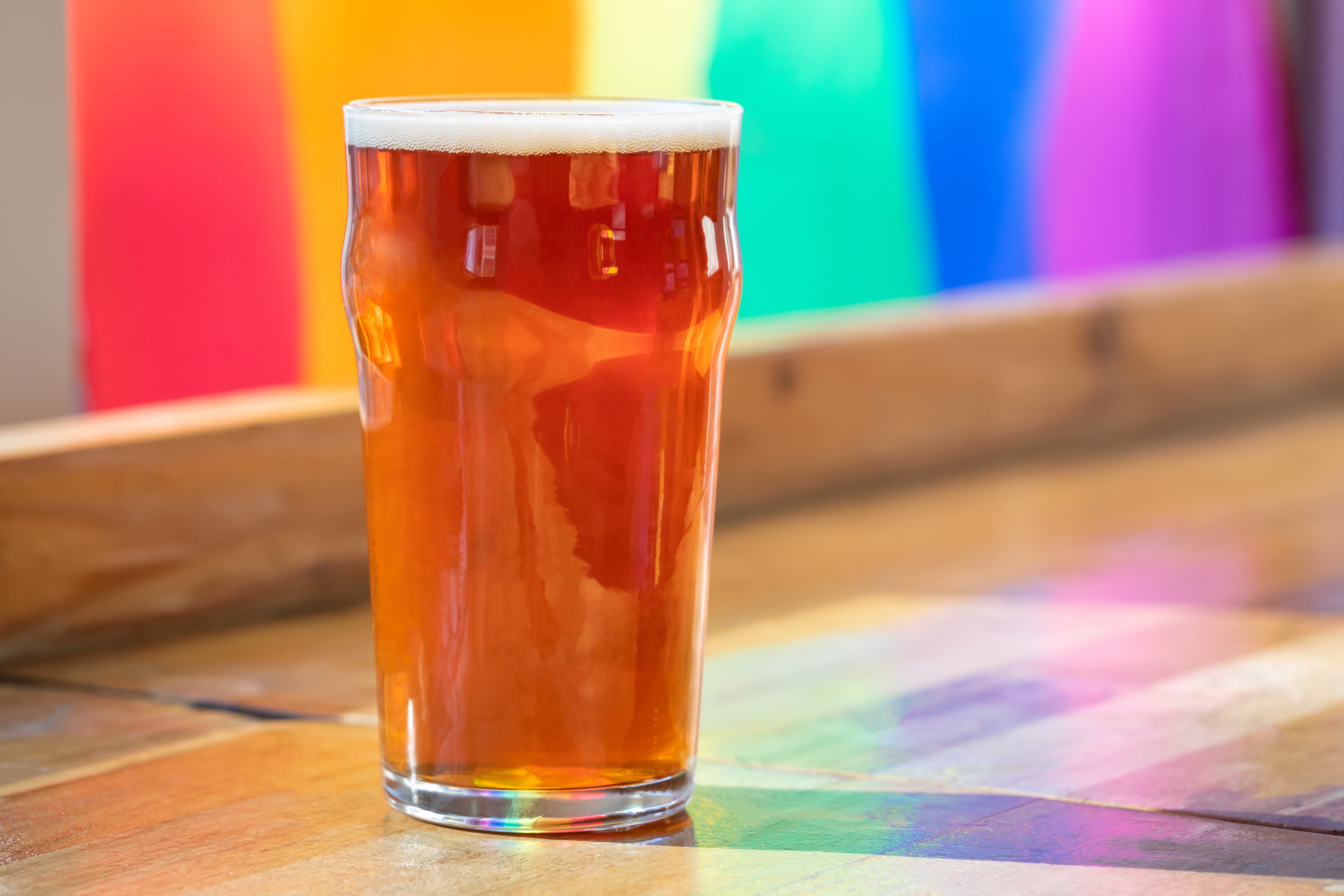 A glass of beer sits on a counter in front of a rainbow flag