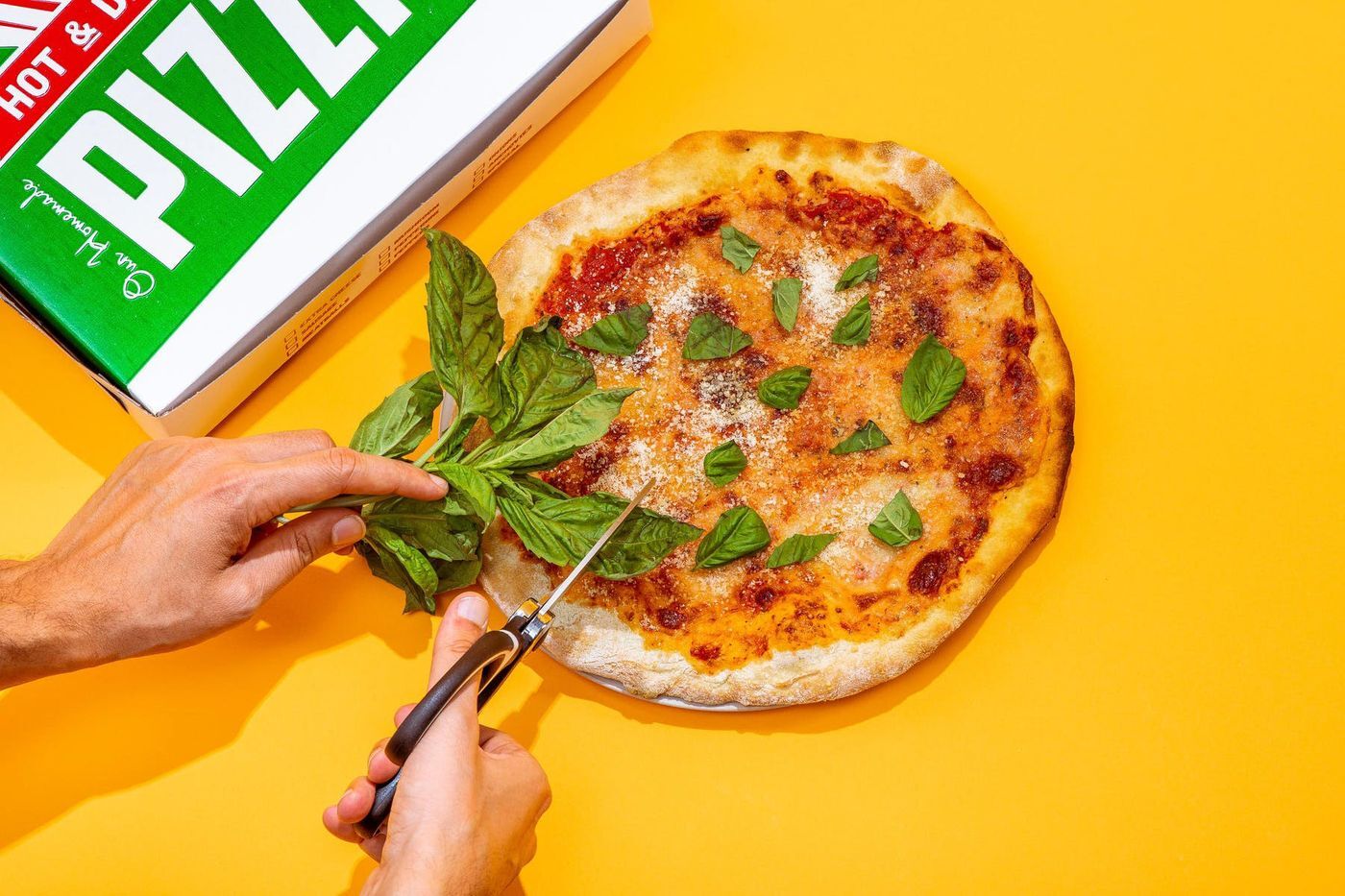 Using scissors, a person cuts basil onto a pizza