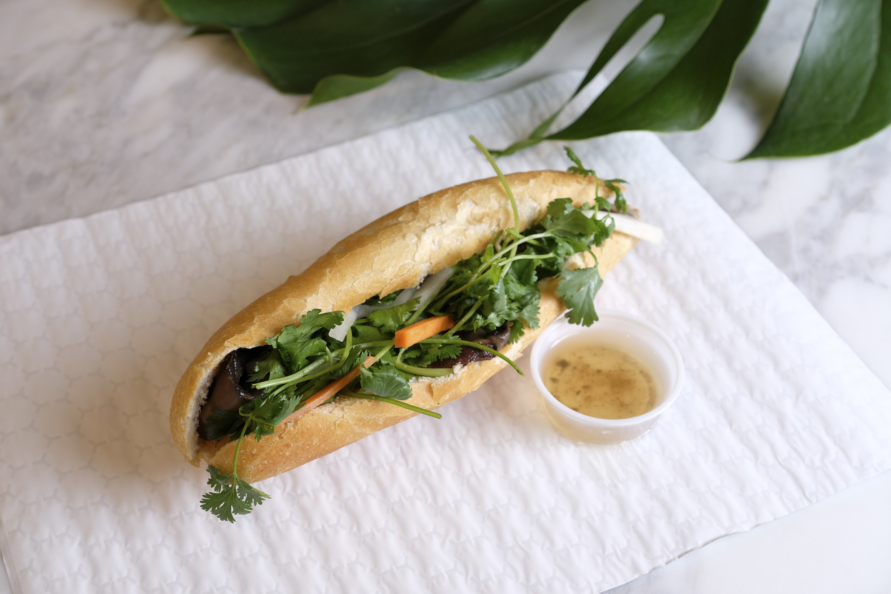 sandwich filled with items and topped with cilantro with a dipping sauce on the side
