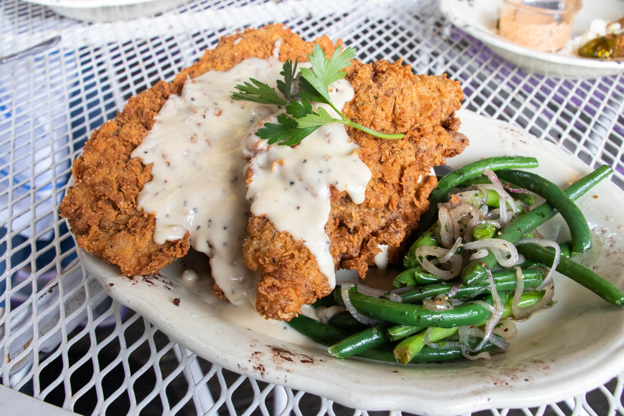 a plate of chicken fried steak topped with white gravy and a side of greens