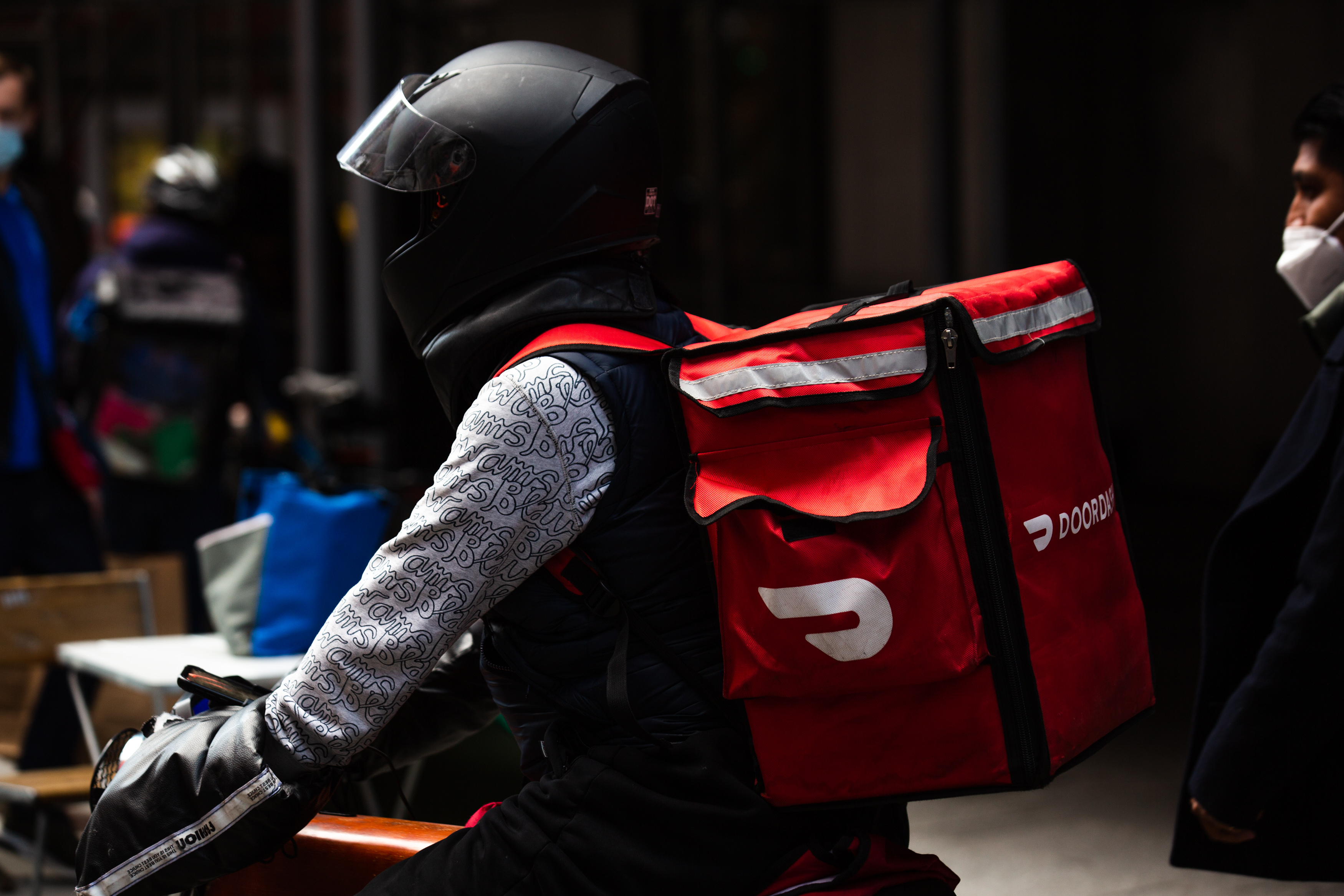 在一个送货人的特写镜头有一个黑摩托车盔甲的和doordash背包外面