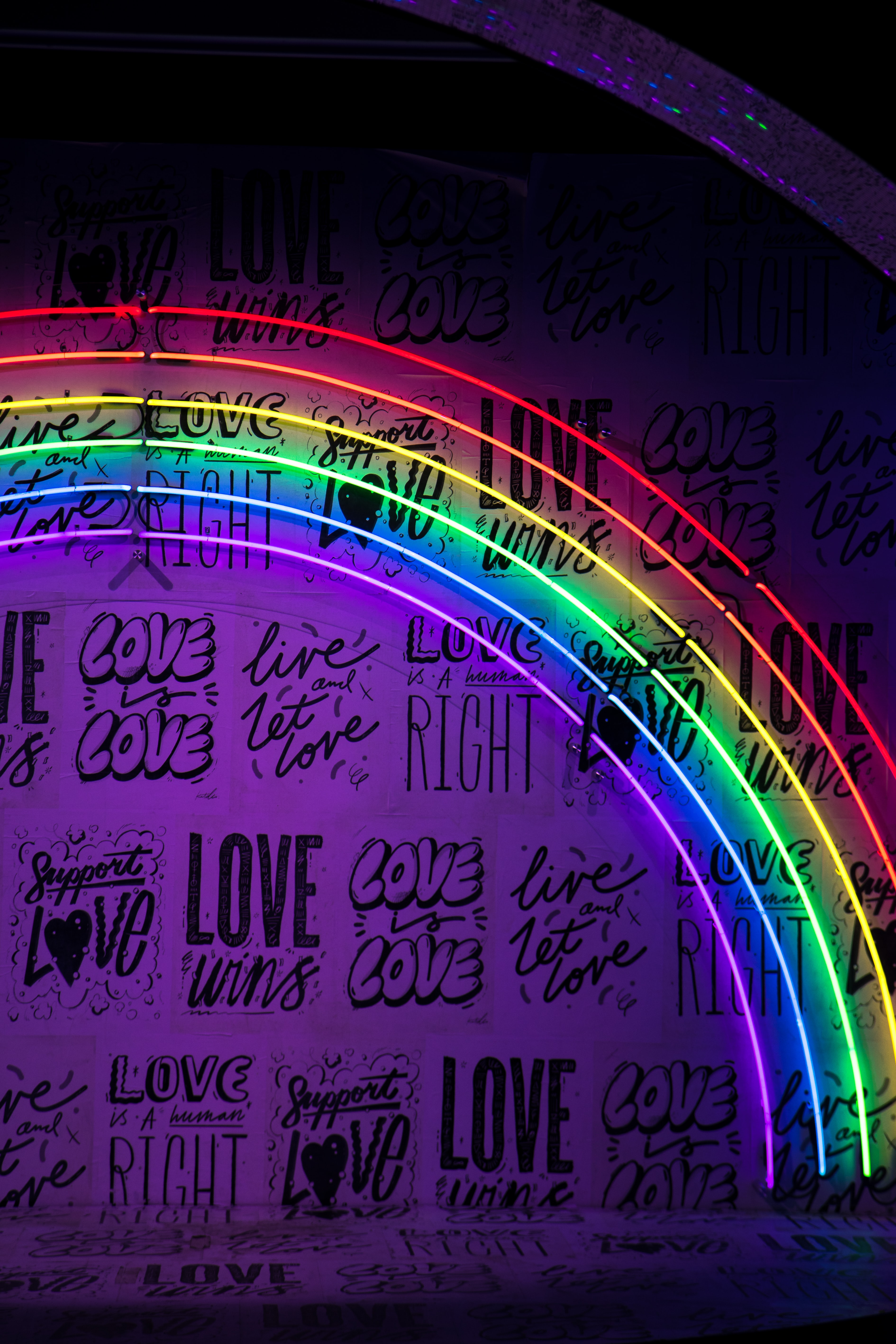 neon rainbow over a white wall with inspirational writing on it
