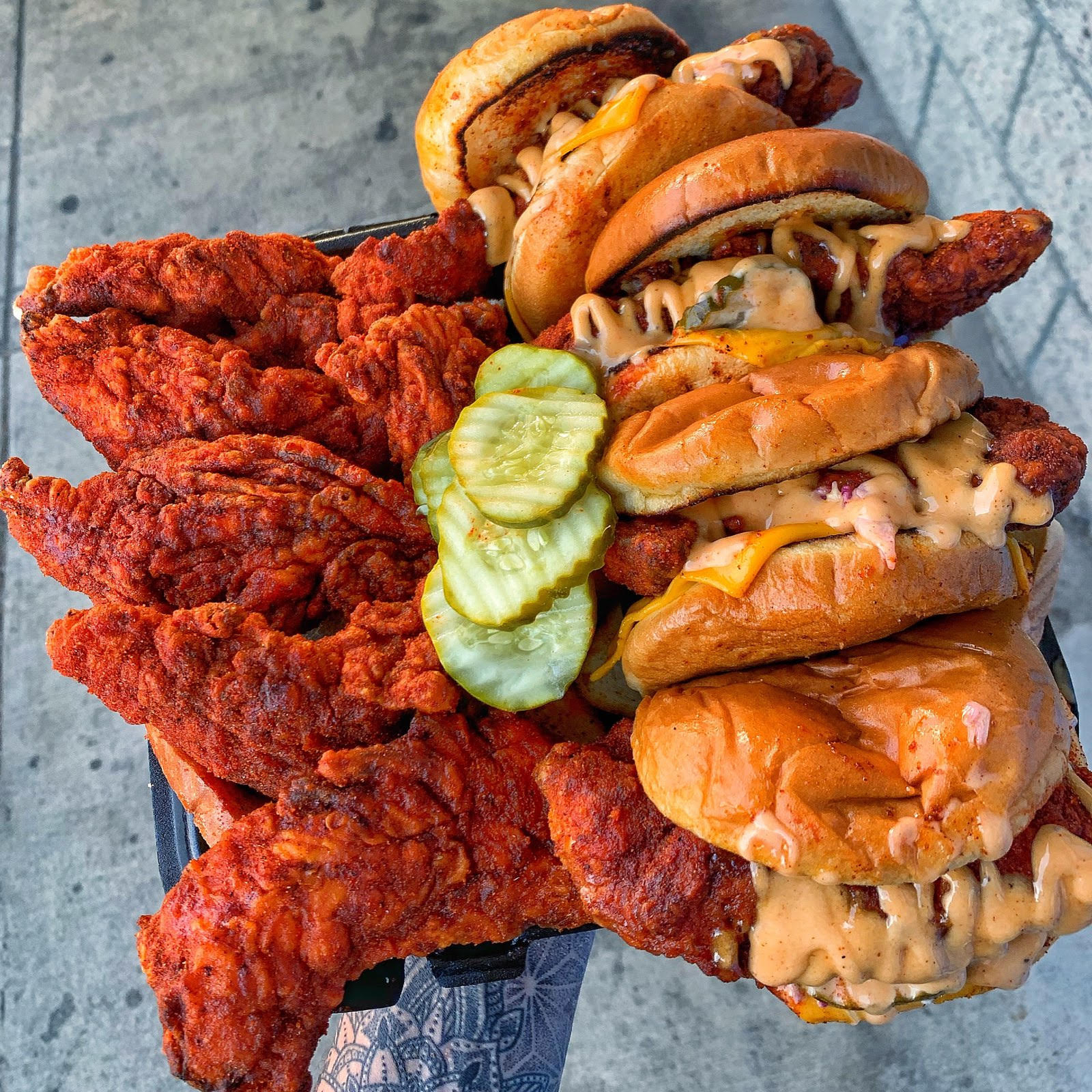 Four chicken tenders on one side of a tray, four sliders on the other, with pickles in the middle