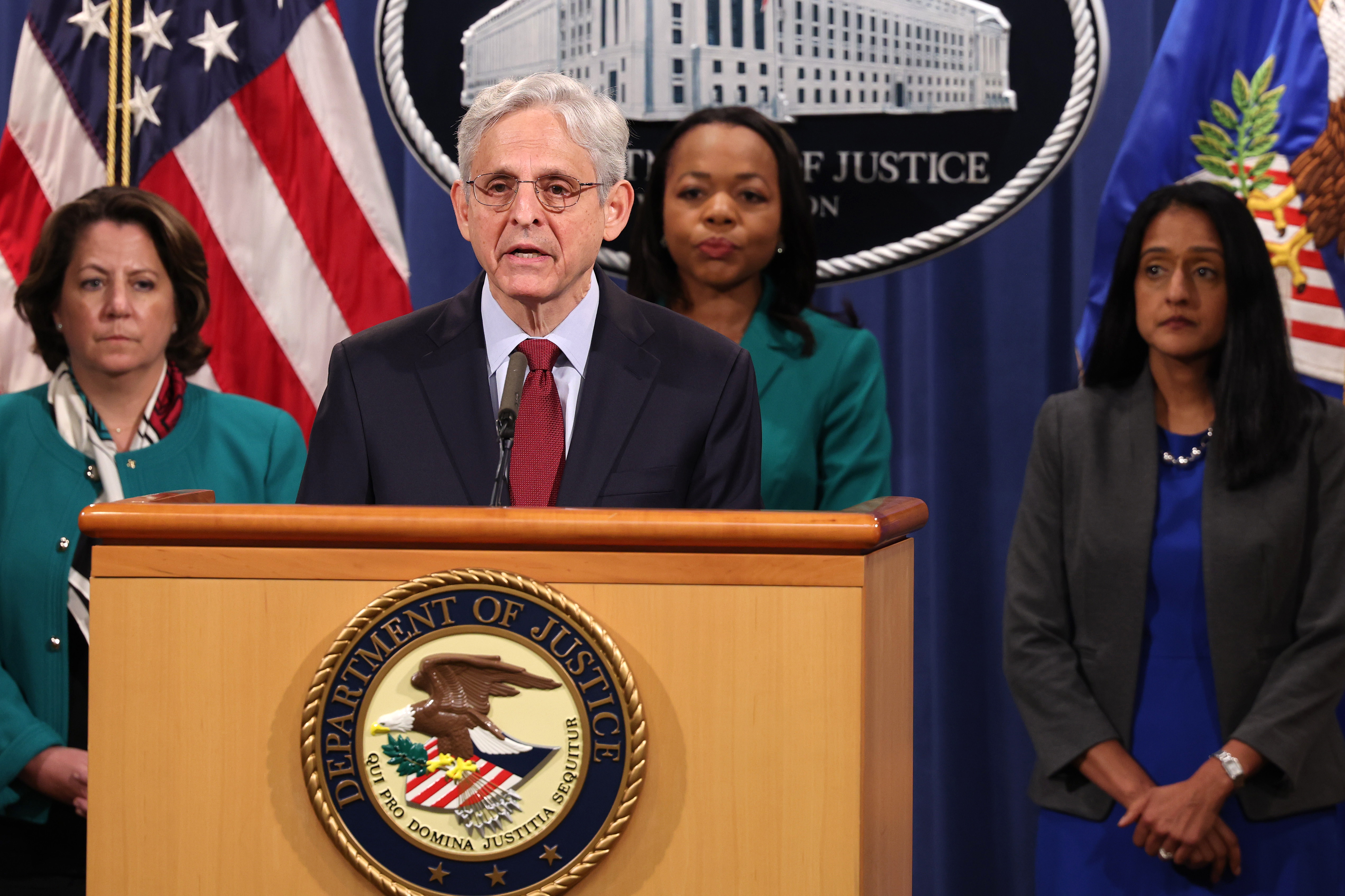 Attorney General Merrick Garland at a lectern with three people standing behind him.