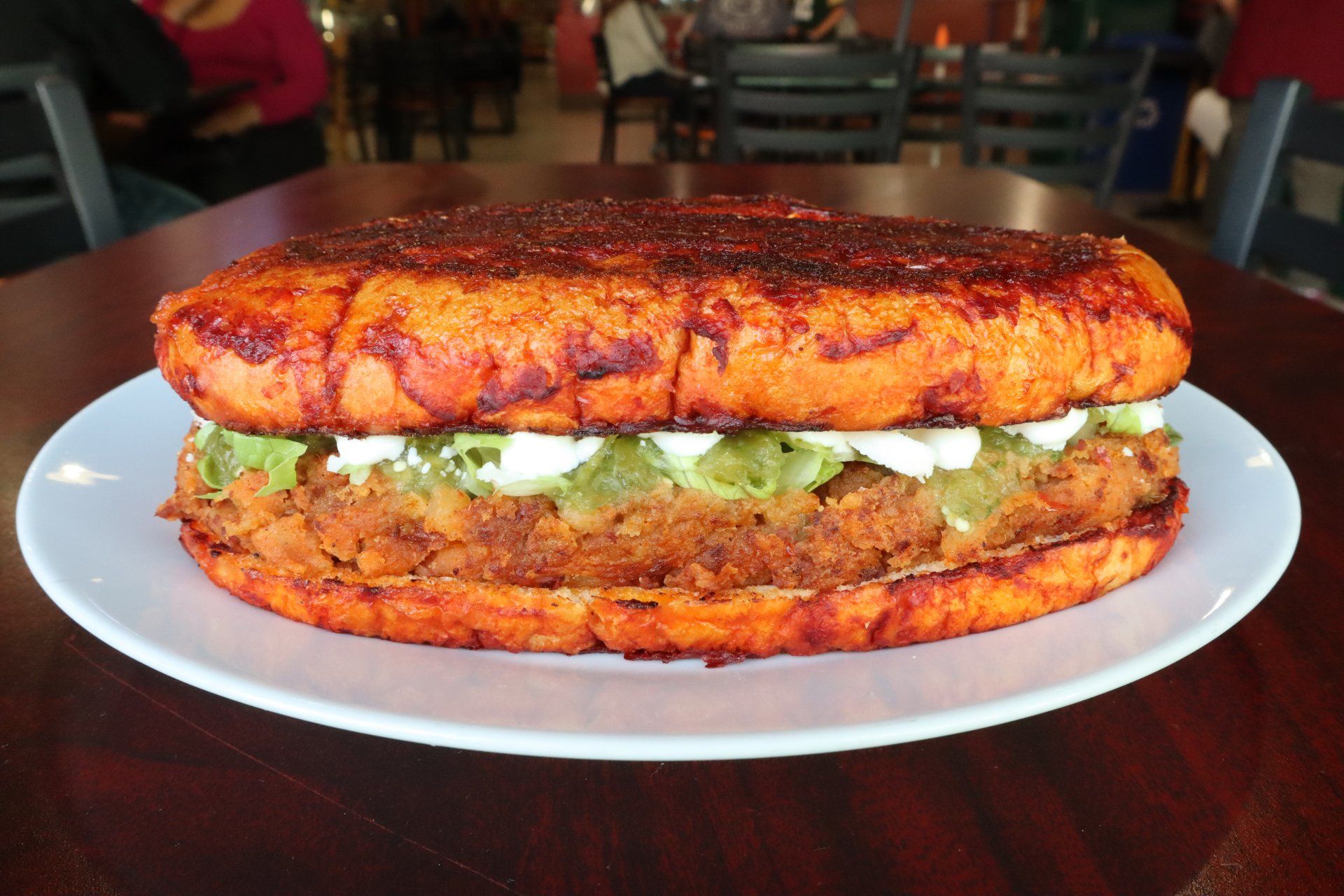 A massive torta, the bread colored by anchiote stuffed with meat, guacamole, and crema