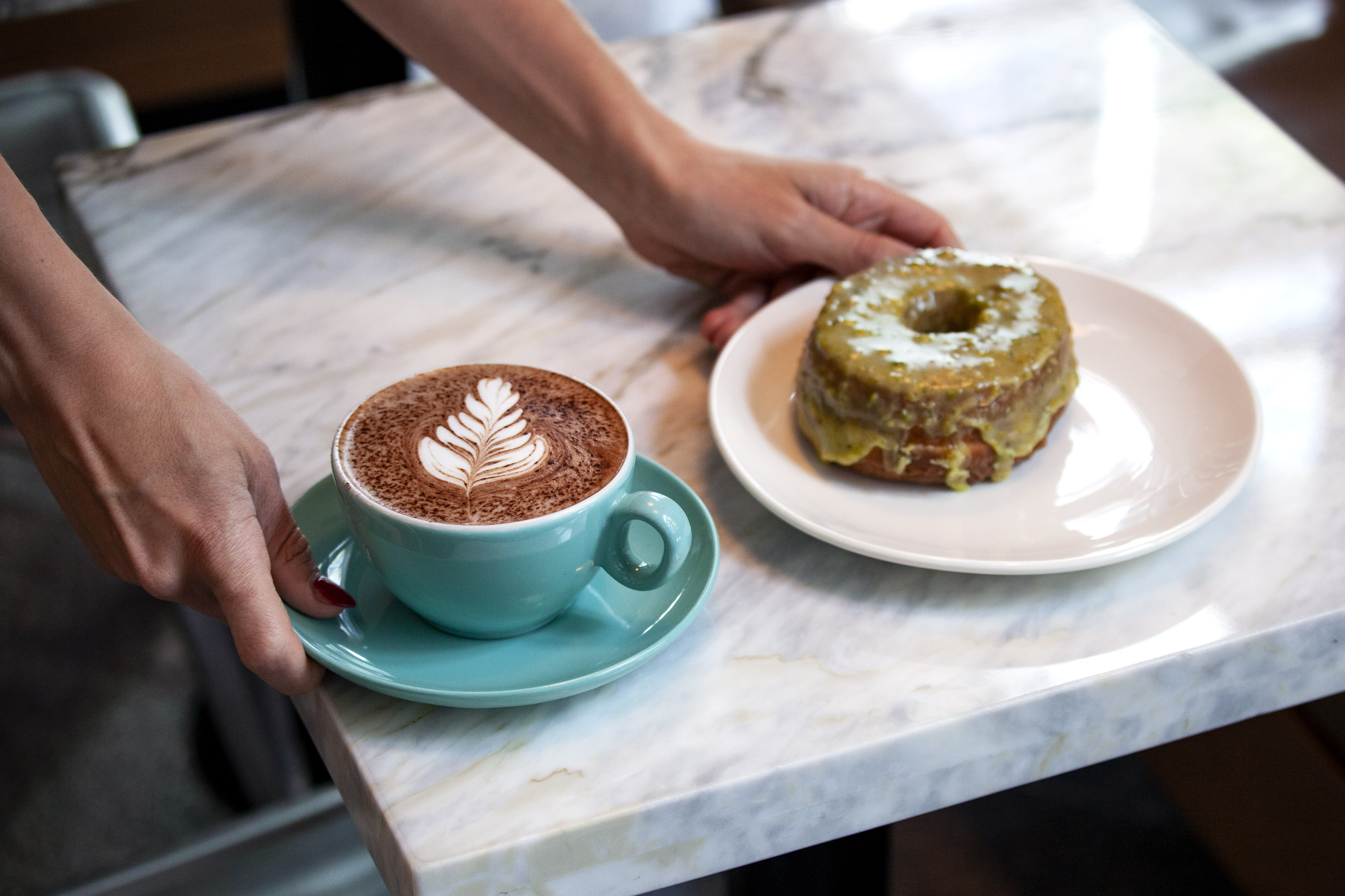 someone holding coffee in aqua blue mug and a doughnut in a plate over a marble table