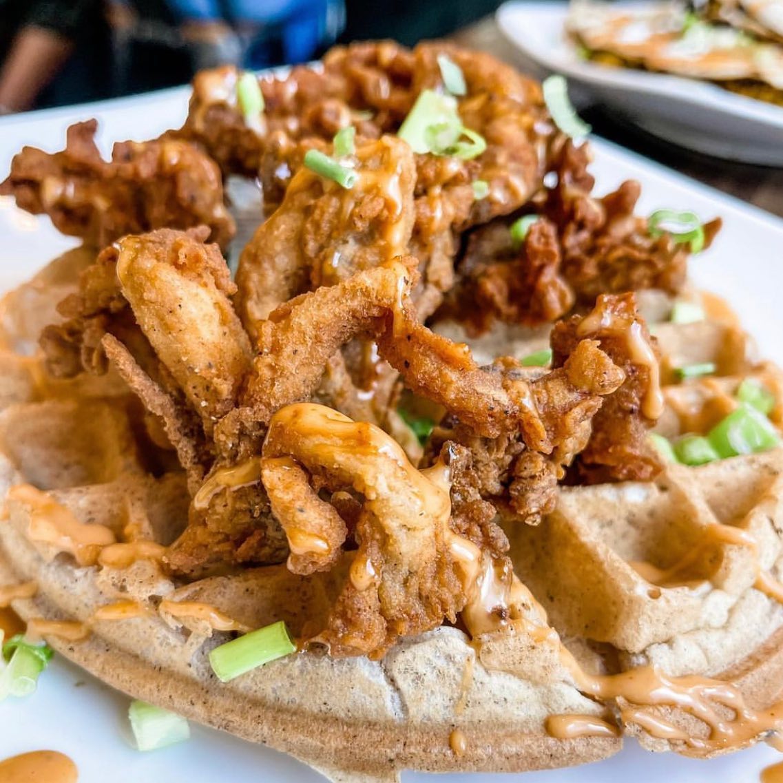 Chicken fried oyster mushrooms atop a Belgian waffle. Some kind of orange sauce is drizzled over top. 