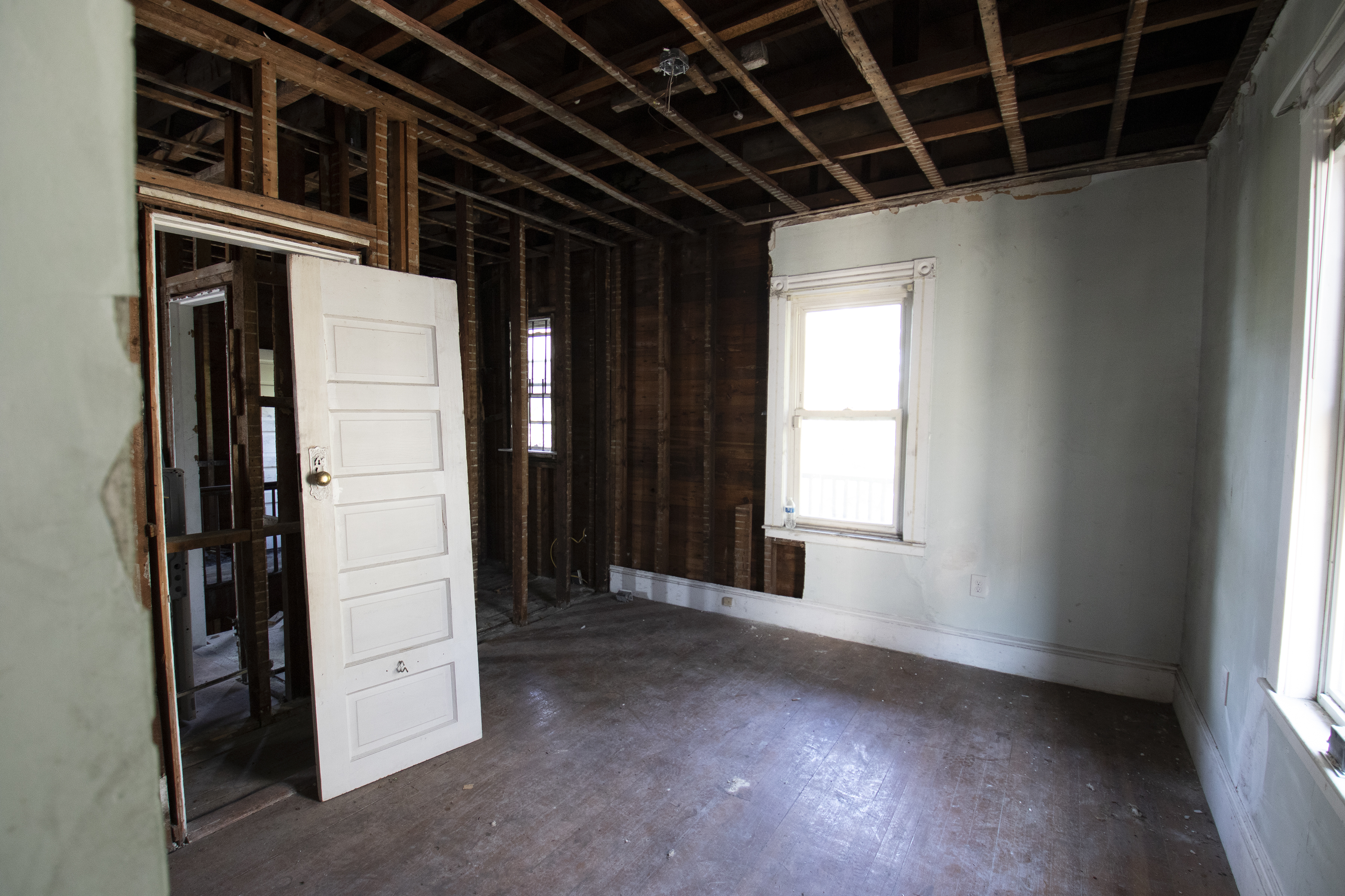 The interior of a house featured on This Old House  Season 42 that sustained fire damage. The left side of the room has all of the drywall removed and a door off of its hinges.