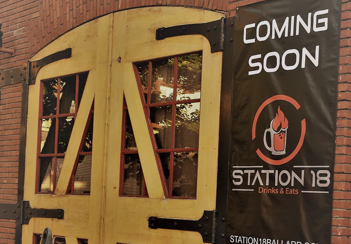 The front of Station 18 Drinks and Eats, with a “coming soon” banner on the side of the brick building