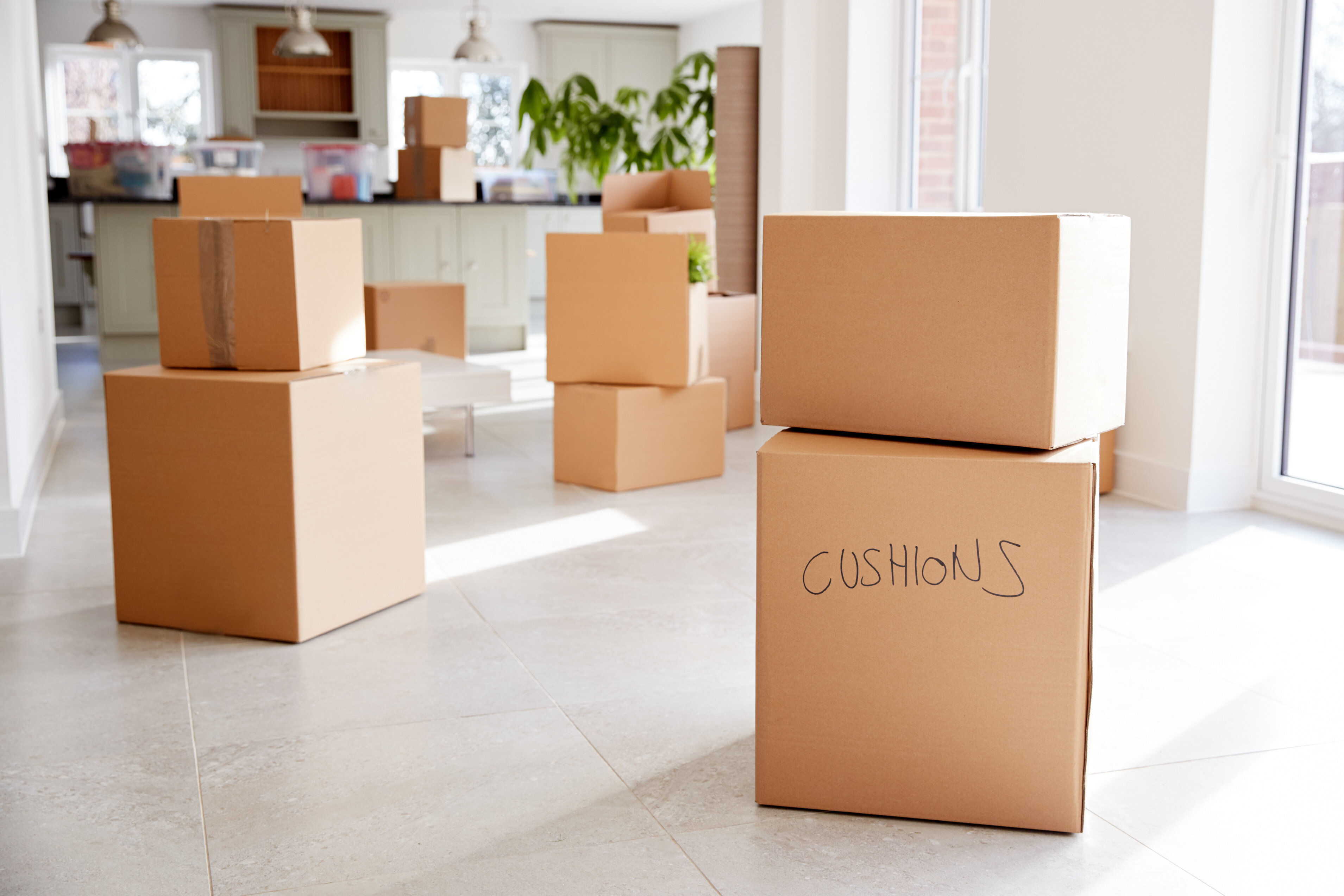Cardboard moving boxes in a bright, white kitchen area of a home. 