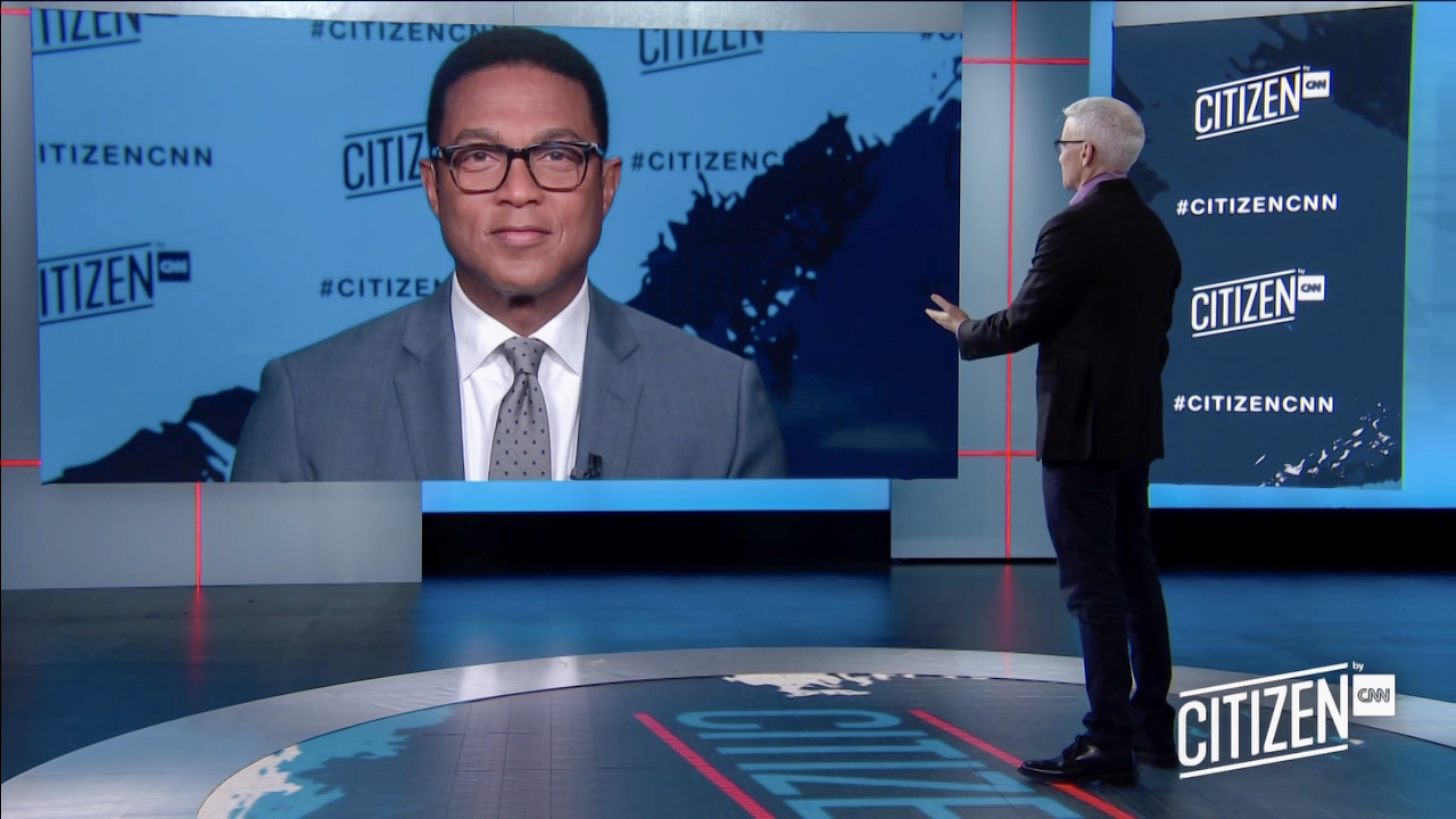 Anderson Cooper stands in the CNN studio speaking with Don Lemon, who appears on a large screen.