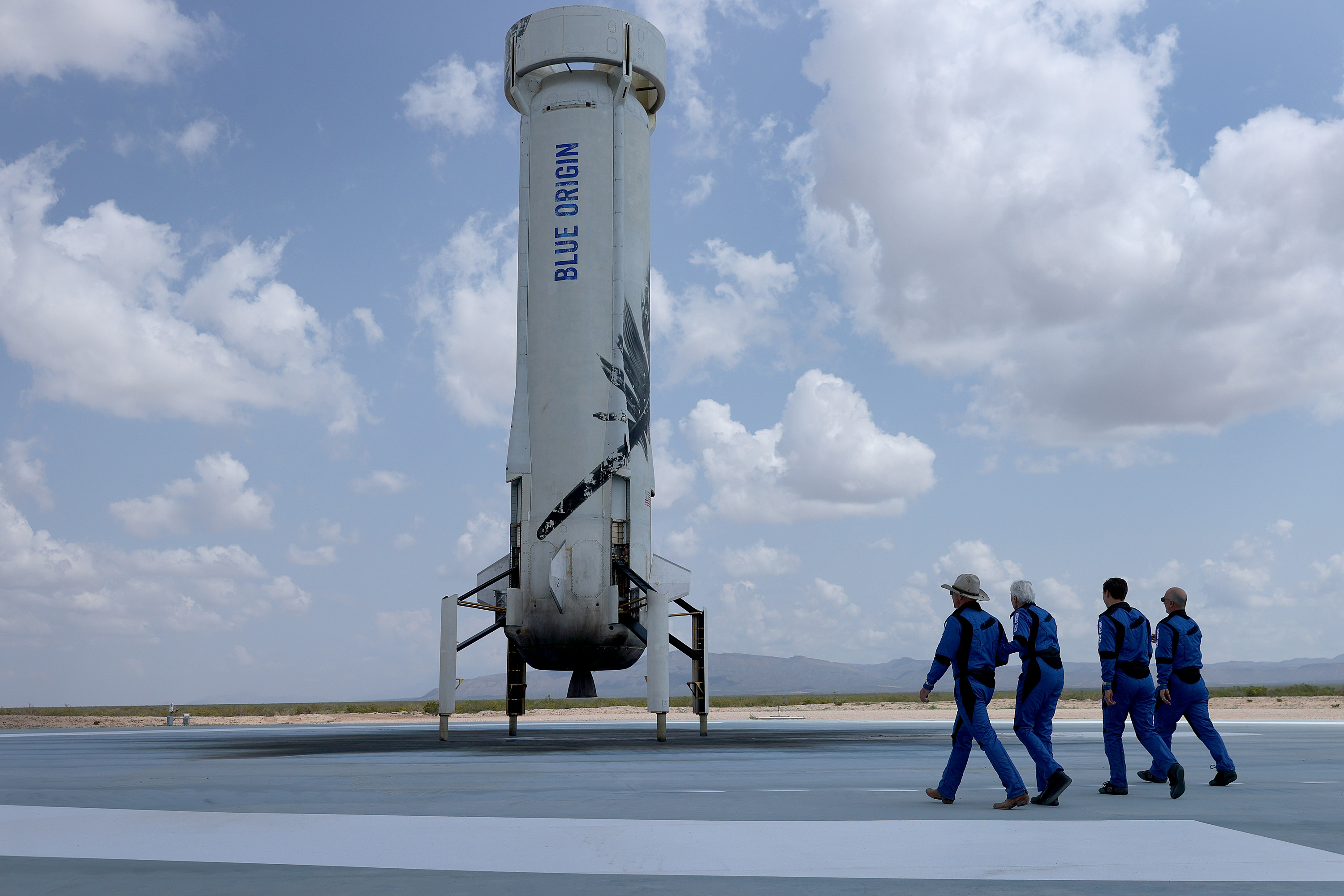 Blue Origin’s New Shepard crew Jeff Bezos, Wally Funk, Oliver Daemen, and Mark Bezos walk near the booster rocket to pose for a picture after their flight into space.