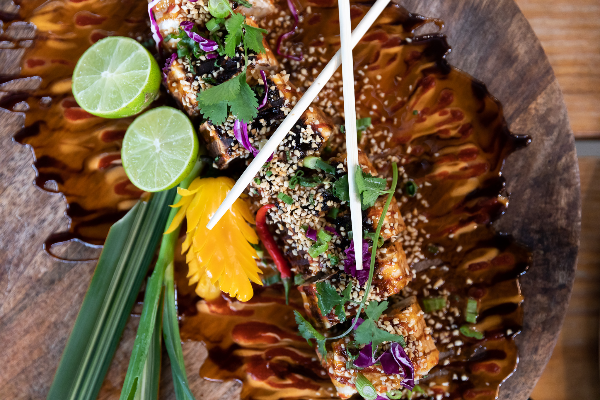 A sliced pad thai roll surrounded by herbs, sliced lime, chopsticks, and a pool of brown sauce.