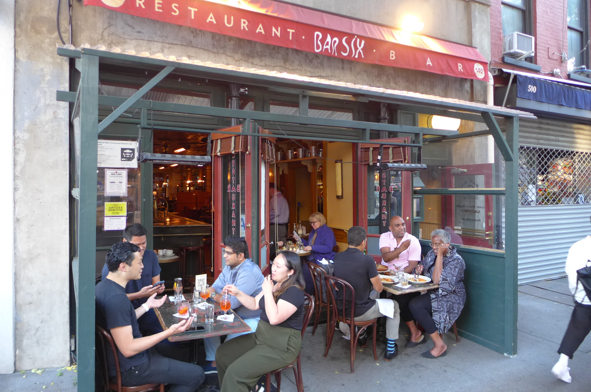 A red awning and two tables of diners sitting in front of the restaurant.