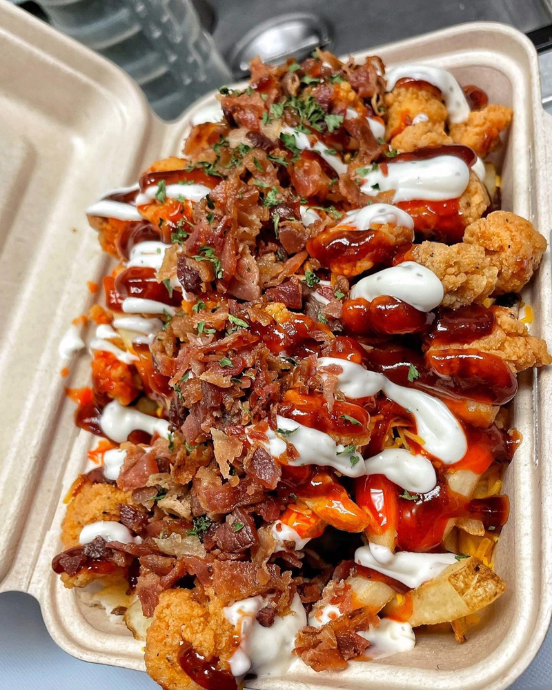 A platter of fries with barbecue sauce, ranch dressing, fried chicken, and bacon