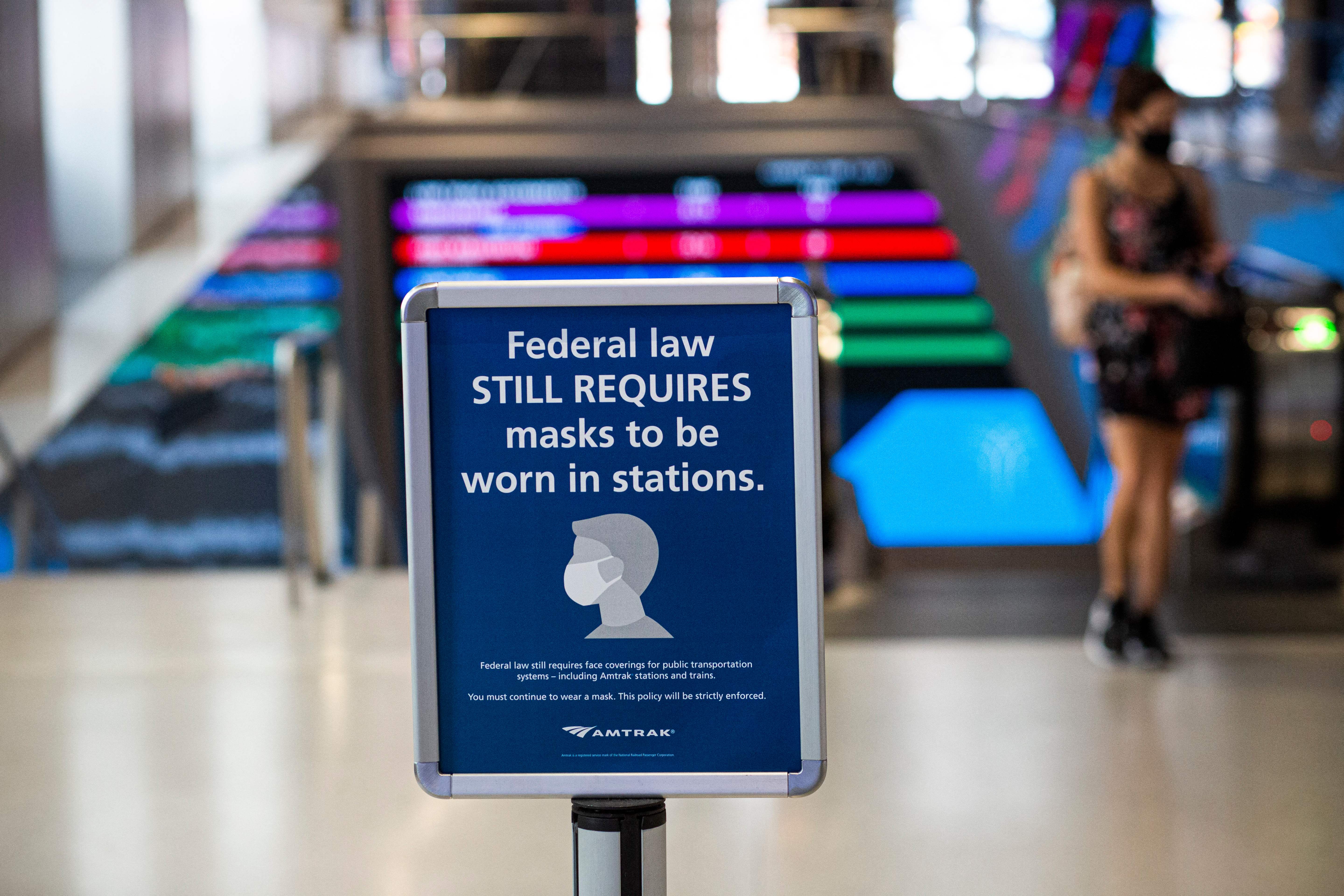 A woman in Penn Station walks past a sign that reads, “Federal law still requires masks to be worn in stations.”