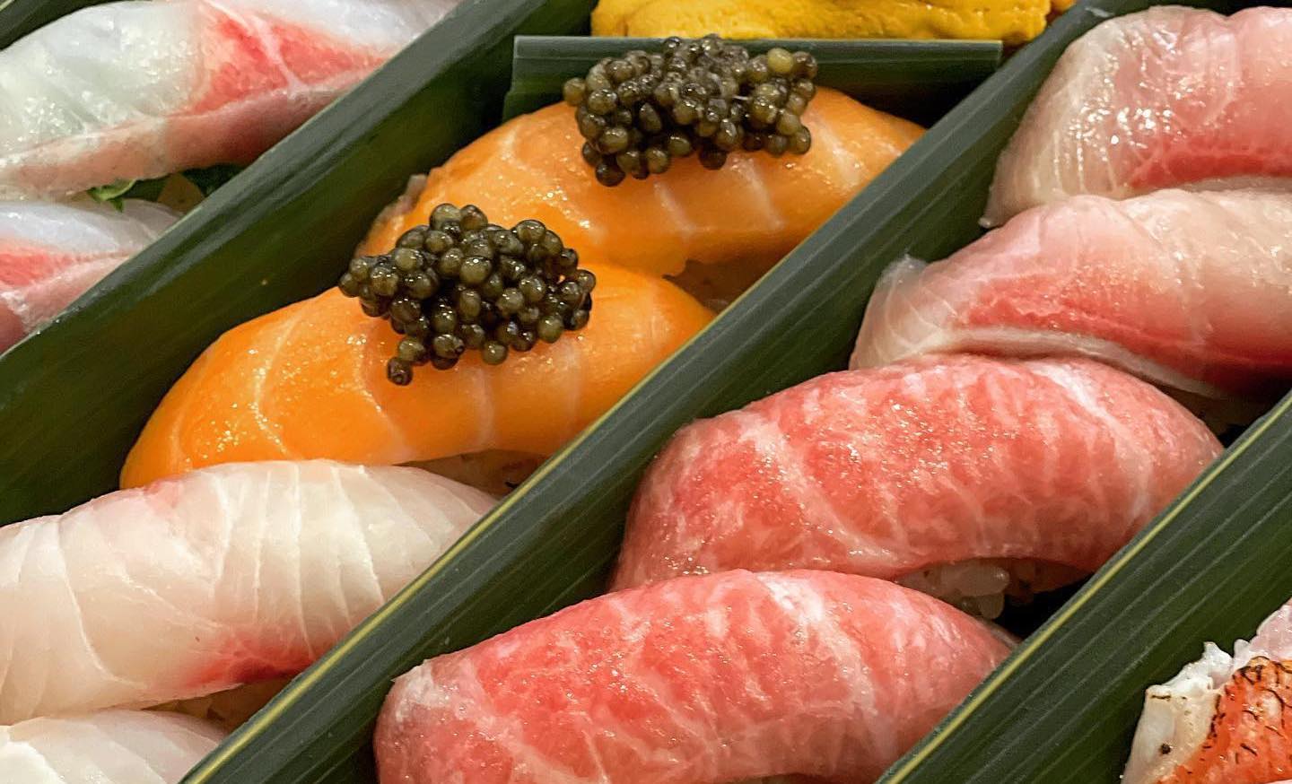 A close up shot of sushi inside of a takeout box, with caviar on top.
