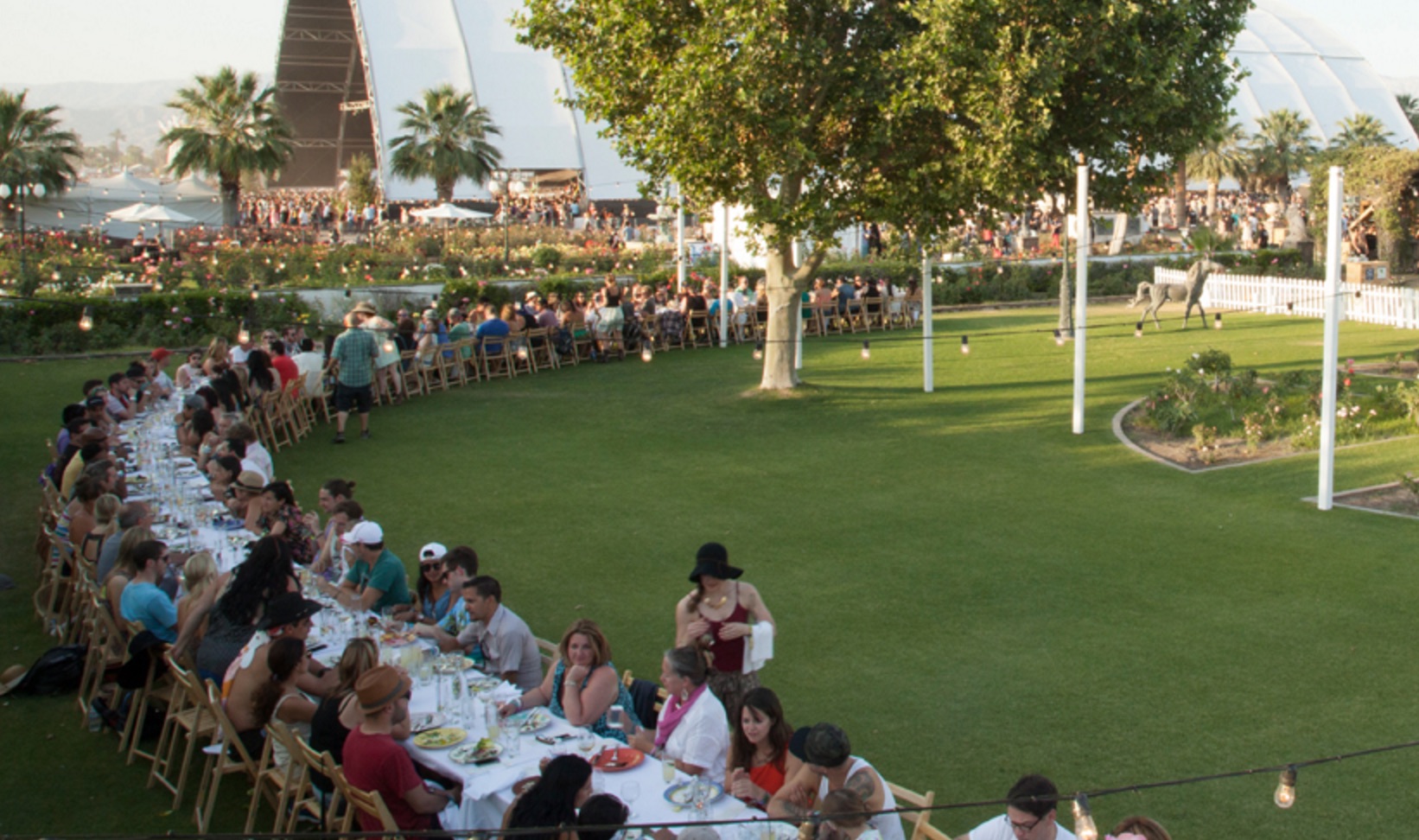 A long tableclothed-table full of diners in an outdoor field