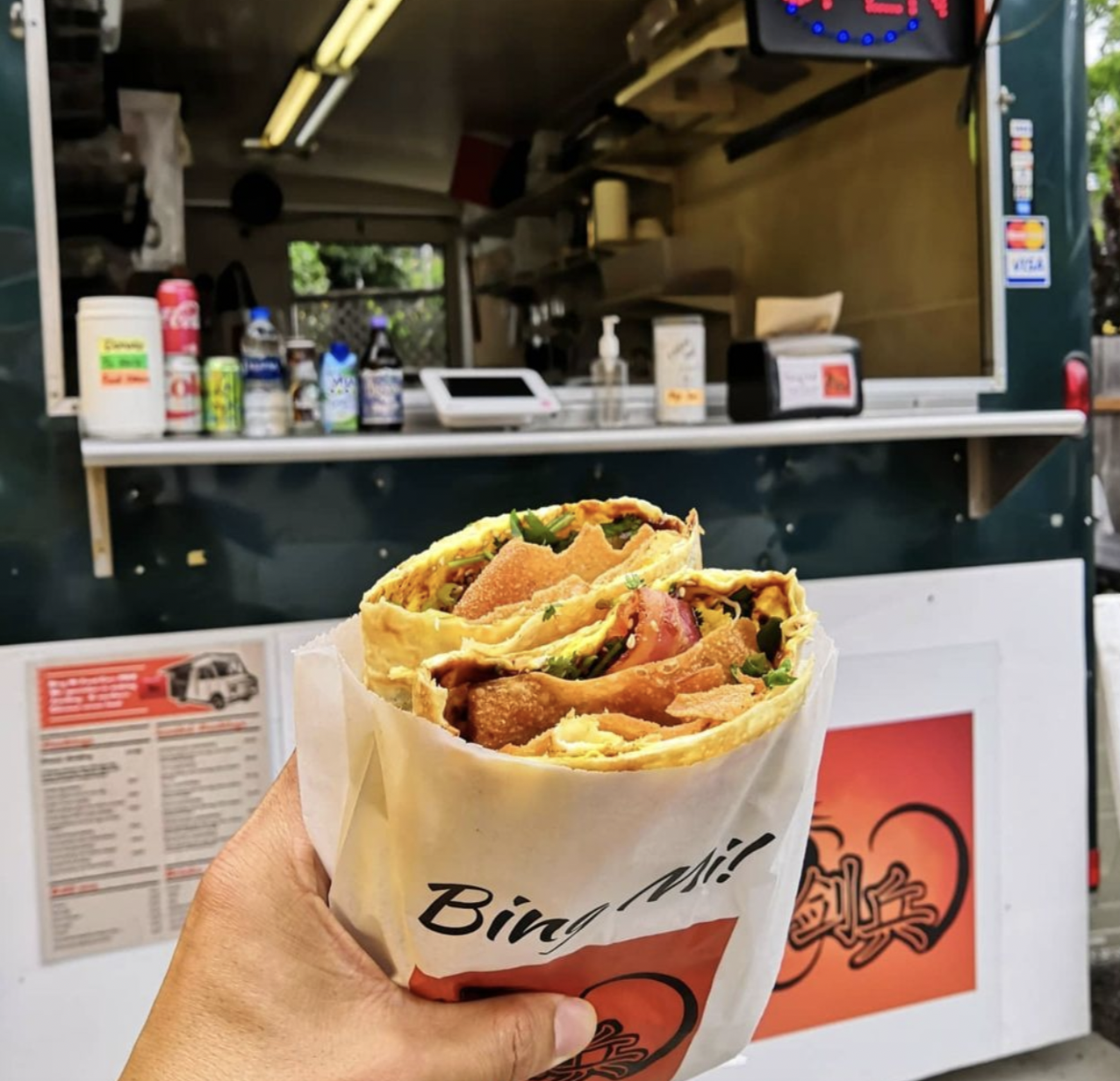 A hand holds a jianbing in front of the Bing Mi cart in Northwest Portland, Oregon.