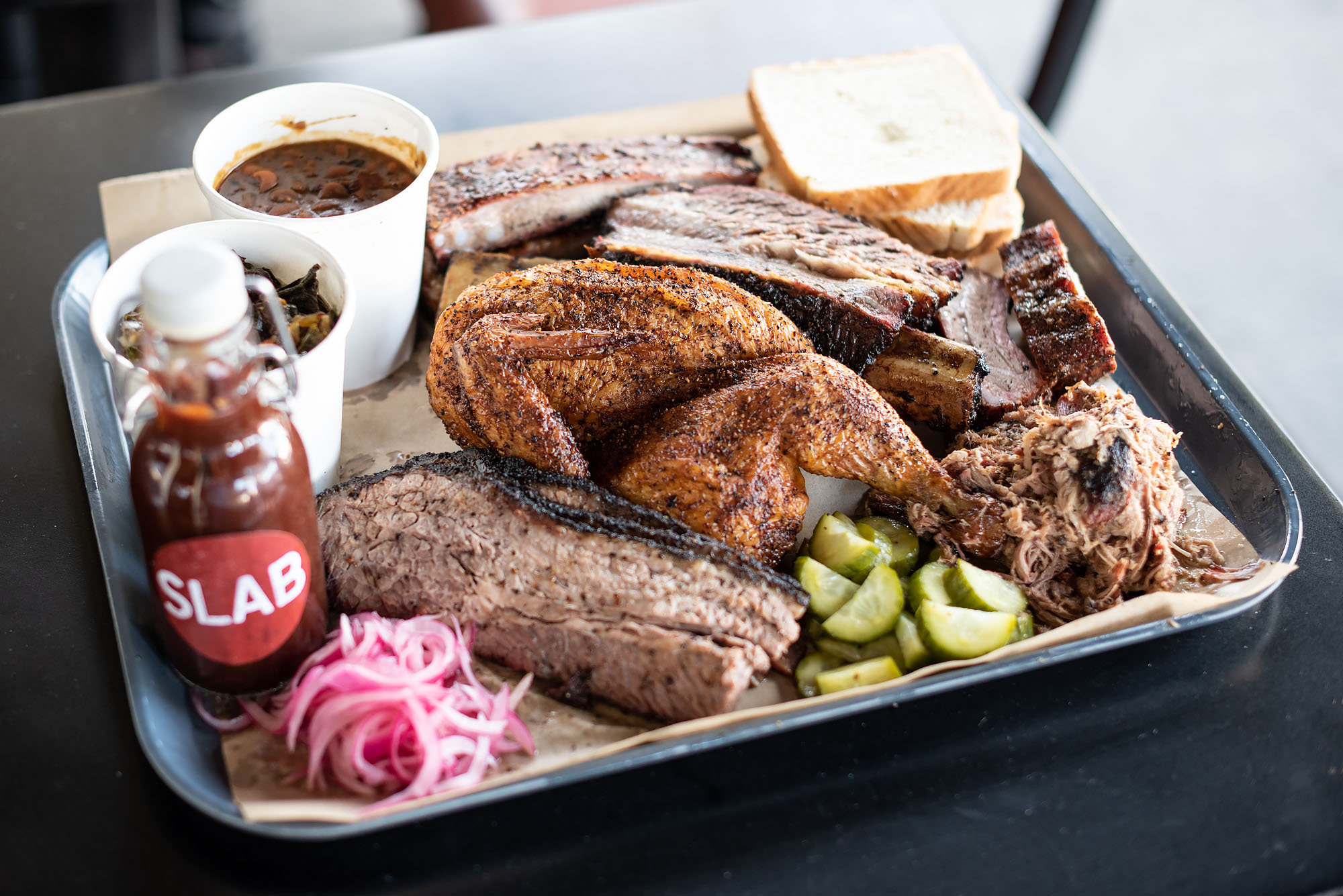 A plate of barbecue, including brisket, smoked chicken, ribs, and sauce.