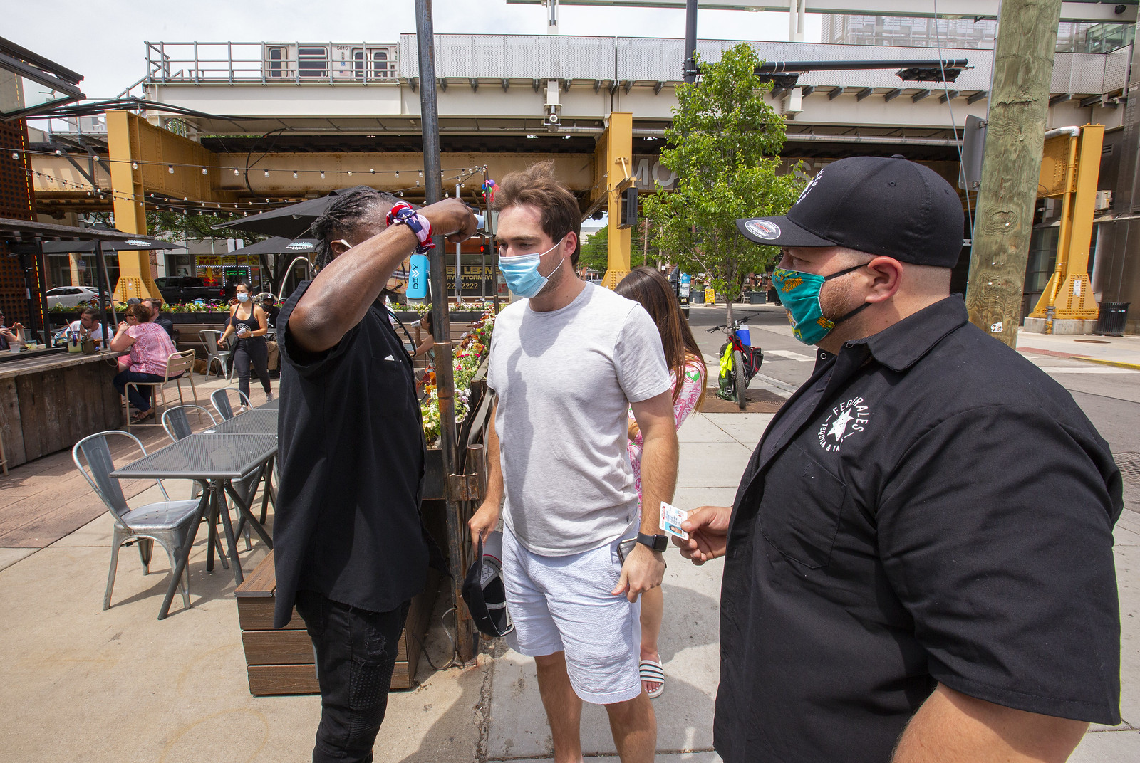 A bouncer with mask outside a bar taking temps of two masked customers.