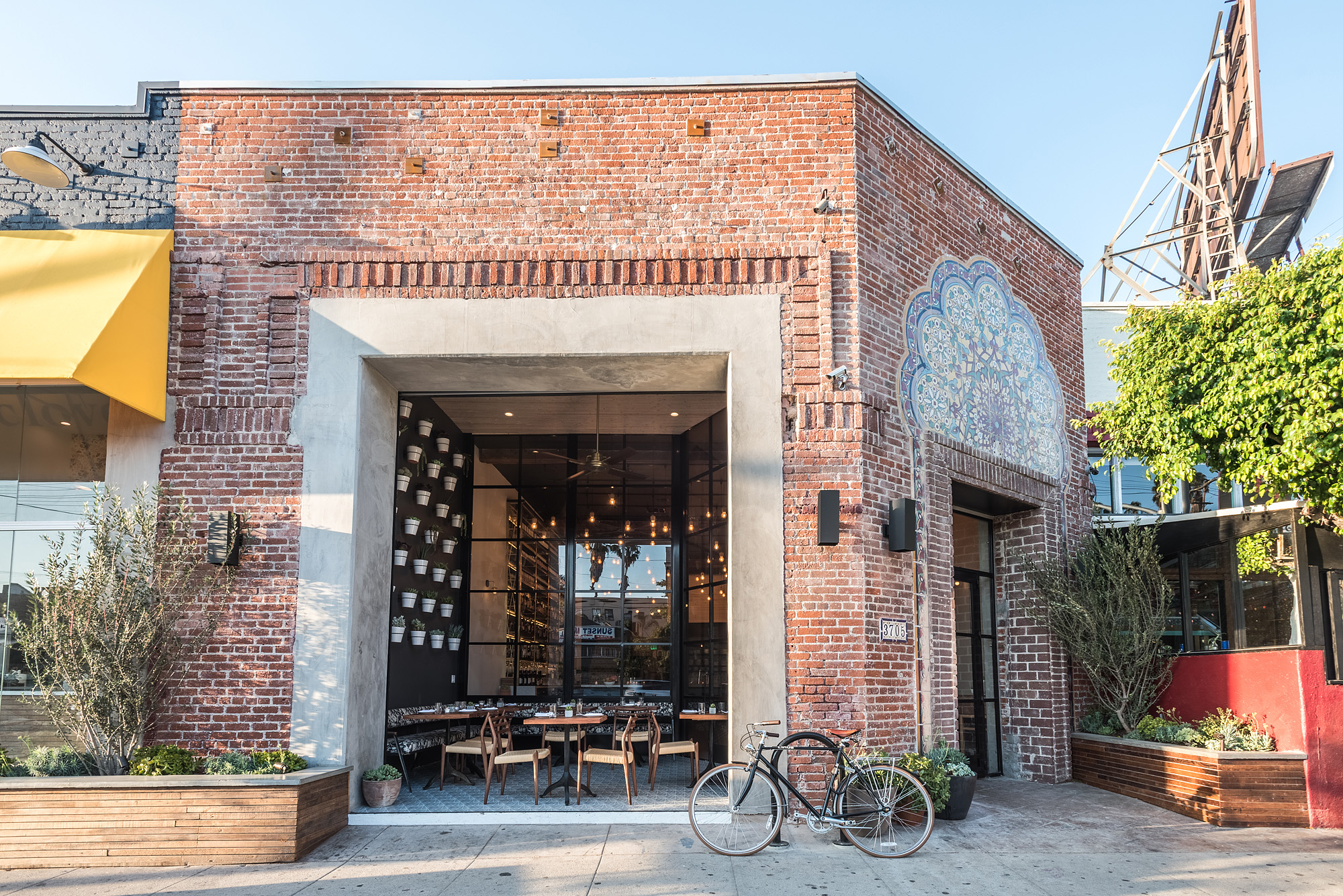 A sunny exterior for a restaurant in Silver Lake, with brick, a small front patio, and yellow awning.