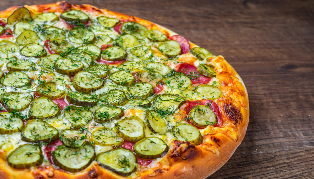 Big dill pizza with Mozzarella cheese, salami, bacon, Tomato sauce, fresh dill, spices and pickled cucumbers on wooden table in the background 