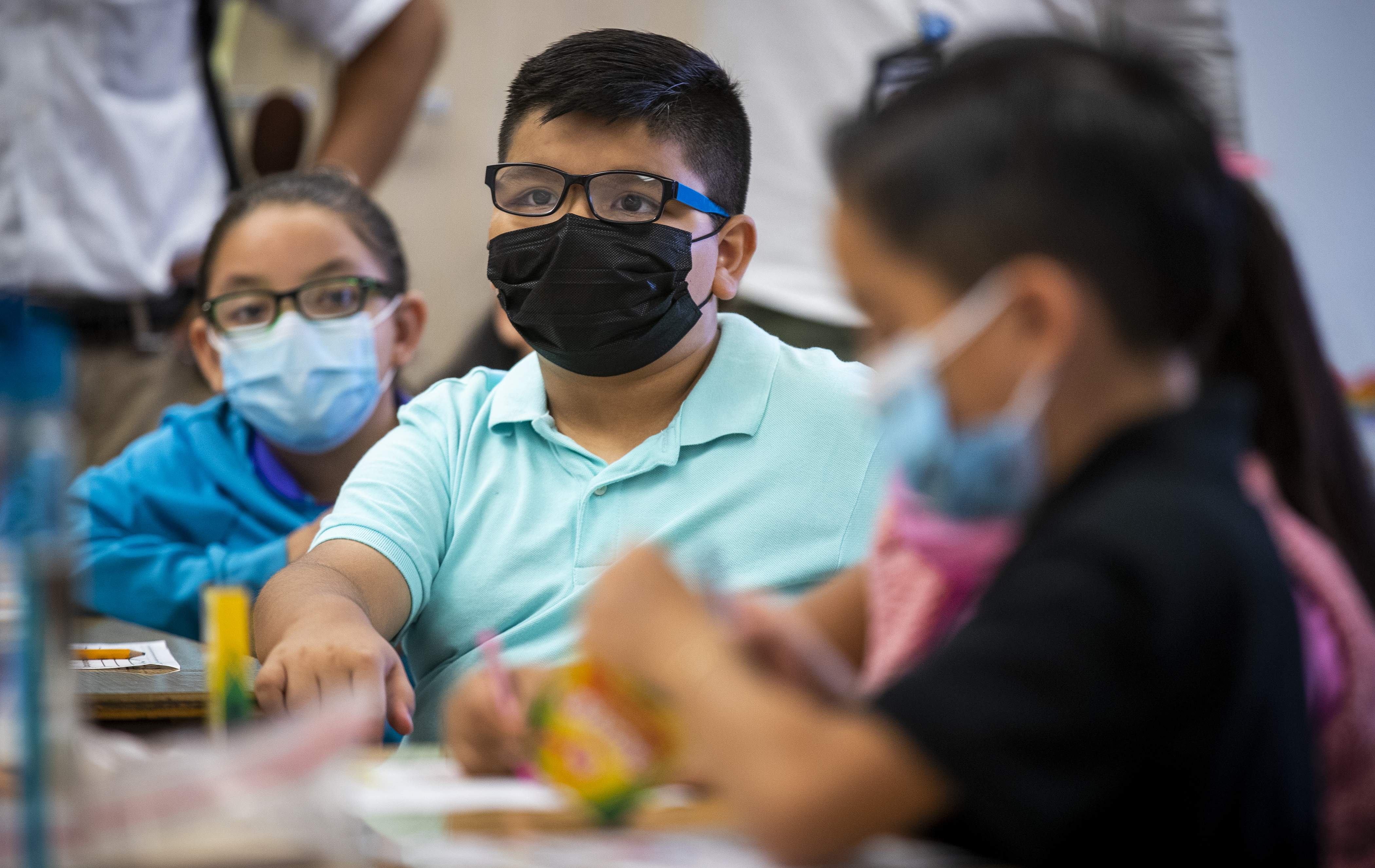 Children wearing masks sit at a classroom table.