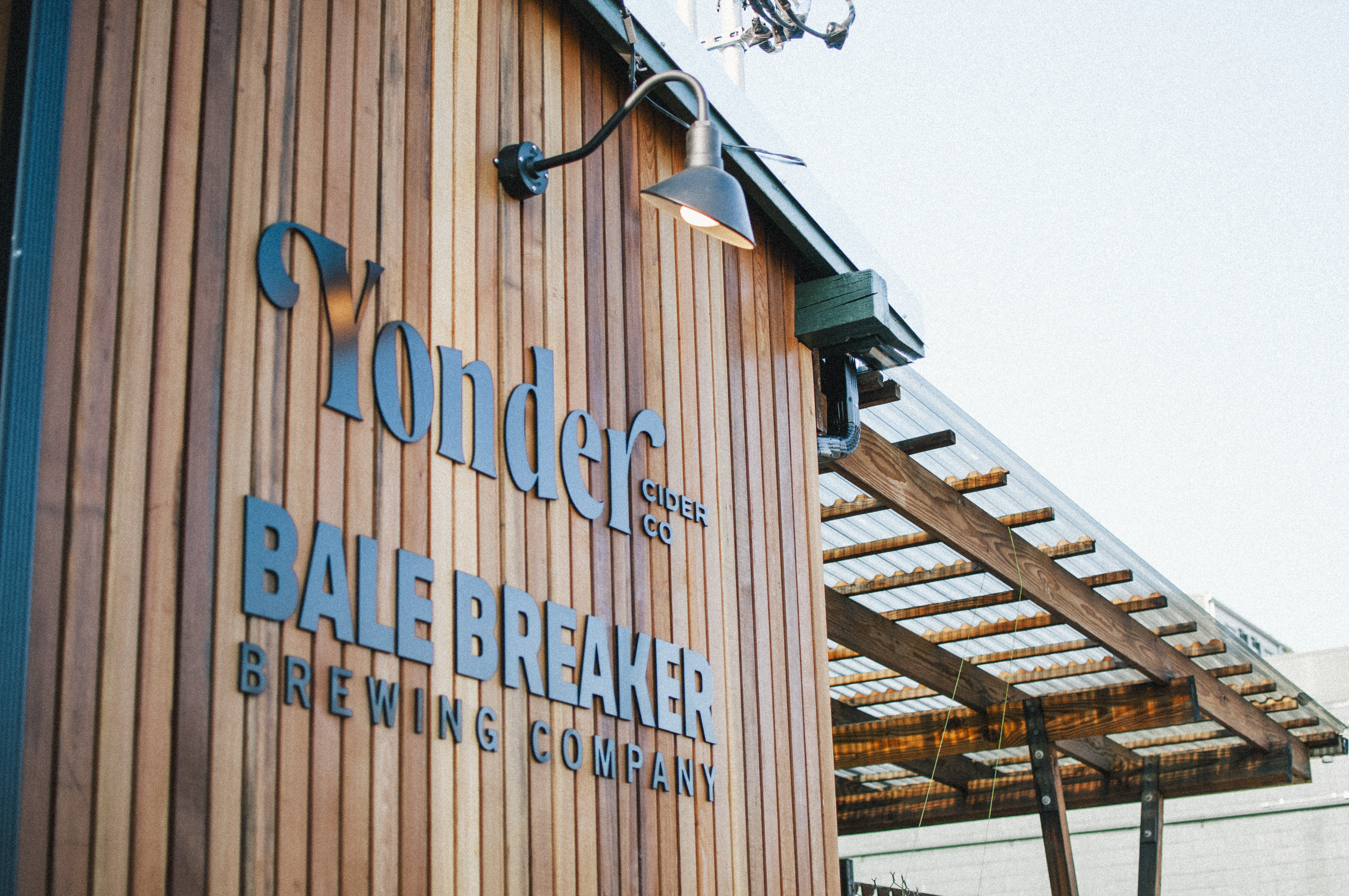The wood facade of Bale Breaker and Yonder taproom. there’s a covered overhang to the right of the main sign displaying the name of each business.