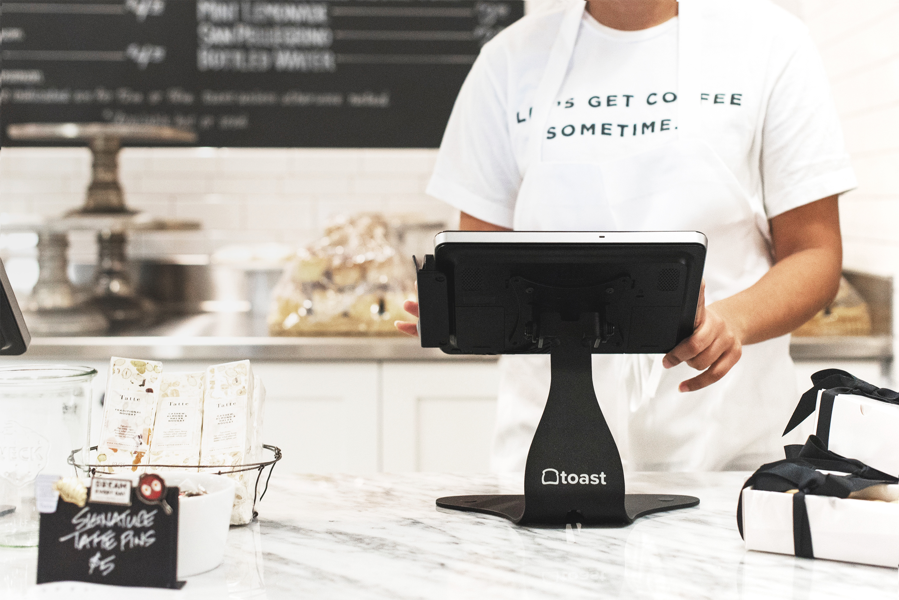 A white marble restaurant counter with a tablet mounted on a stand and a person operating said tablet.