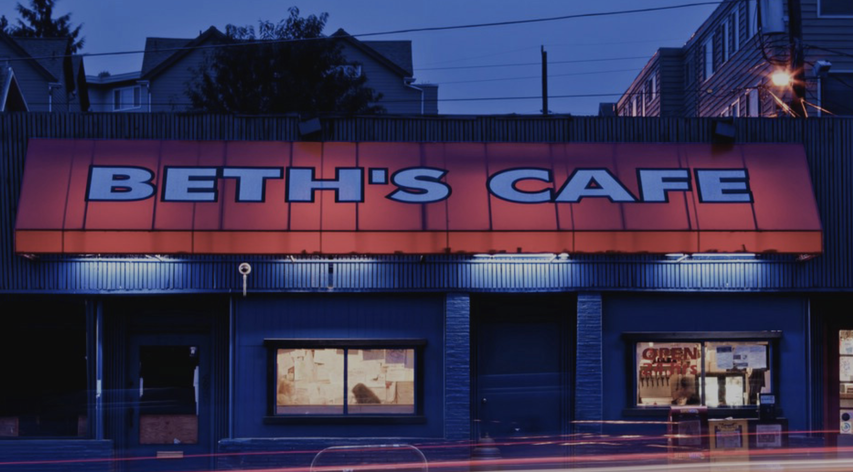 The front of Beth’s Cafe with its red awning backlit at dusk