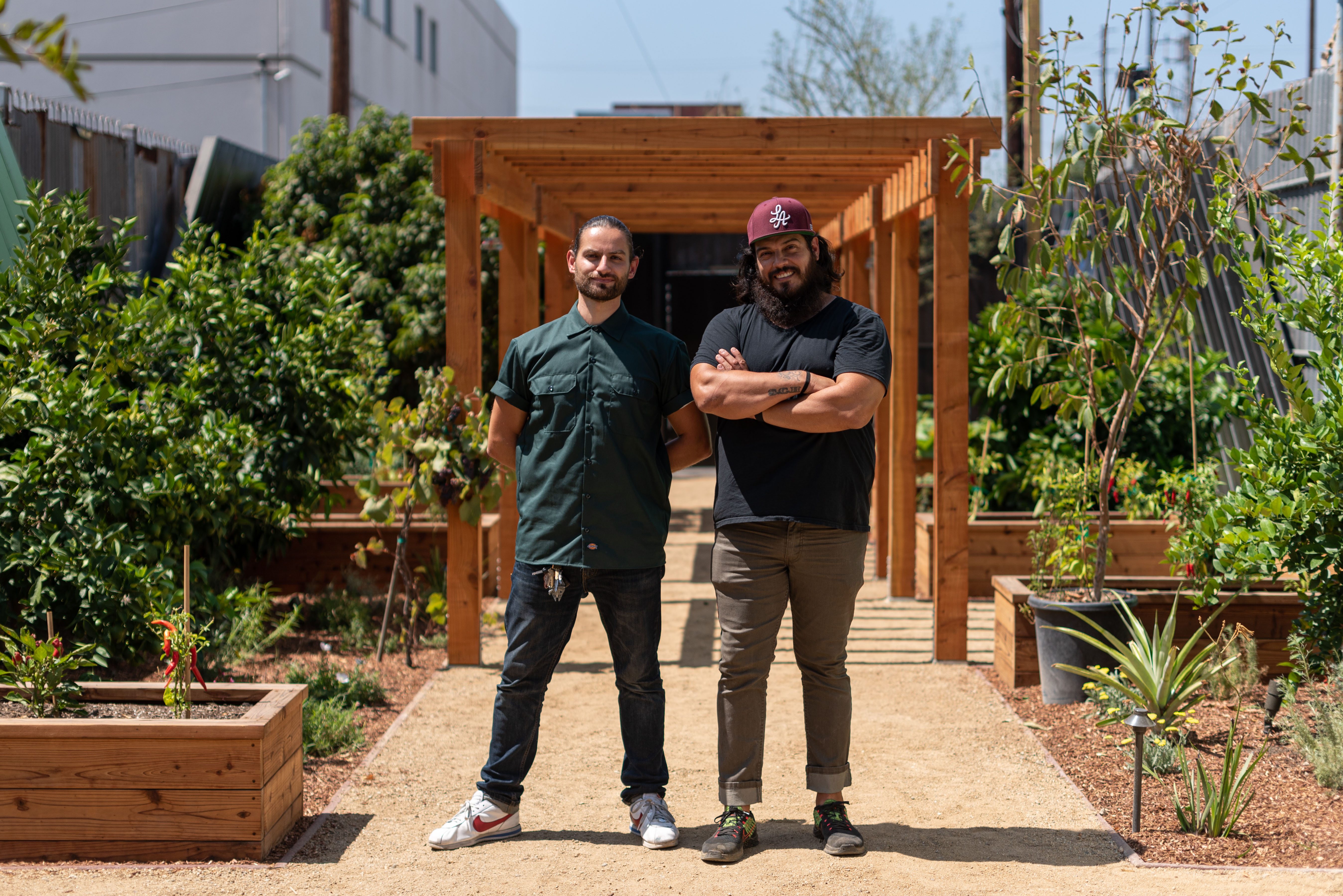 Two men stand in a sunny garden looking directly at camera.