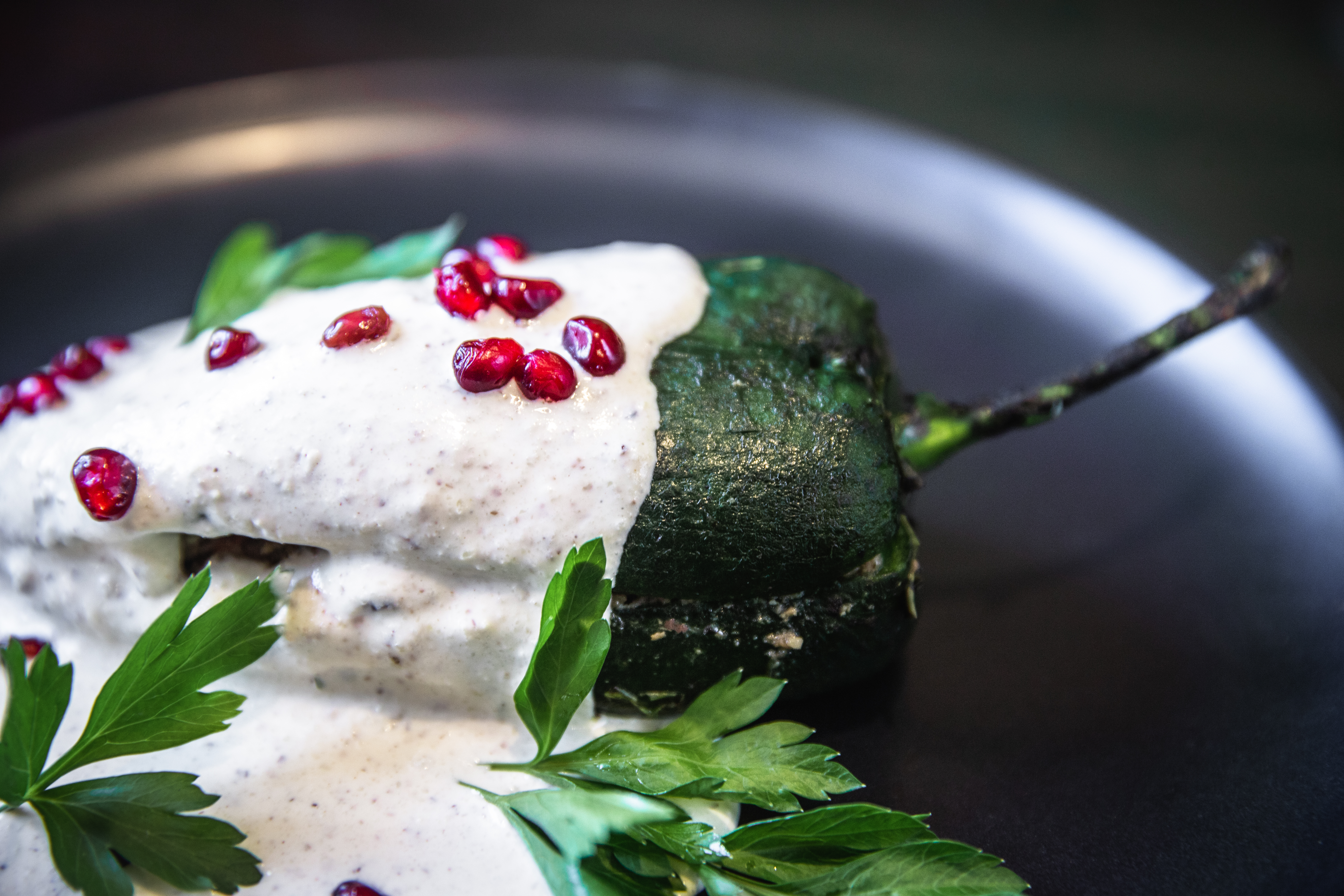 A green chile with cream and pomegranate on a black dish.