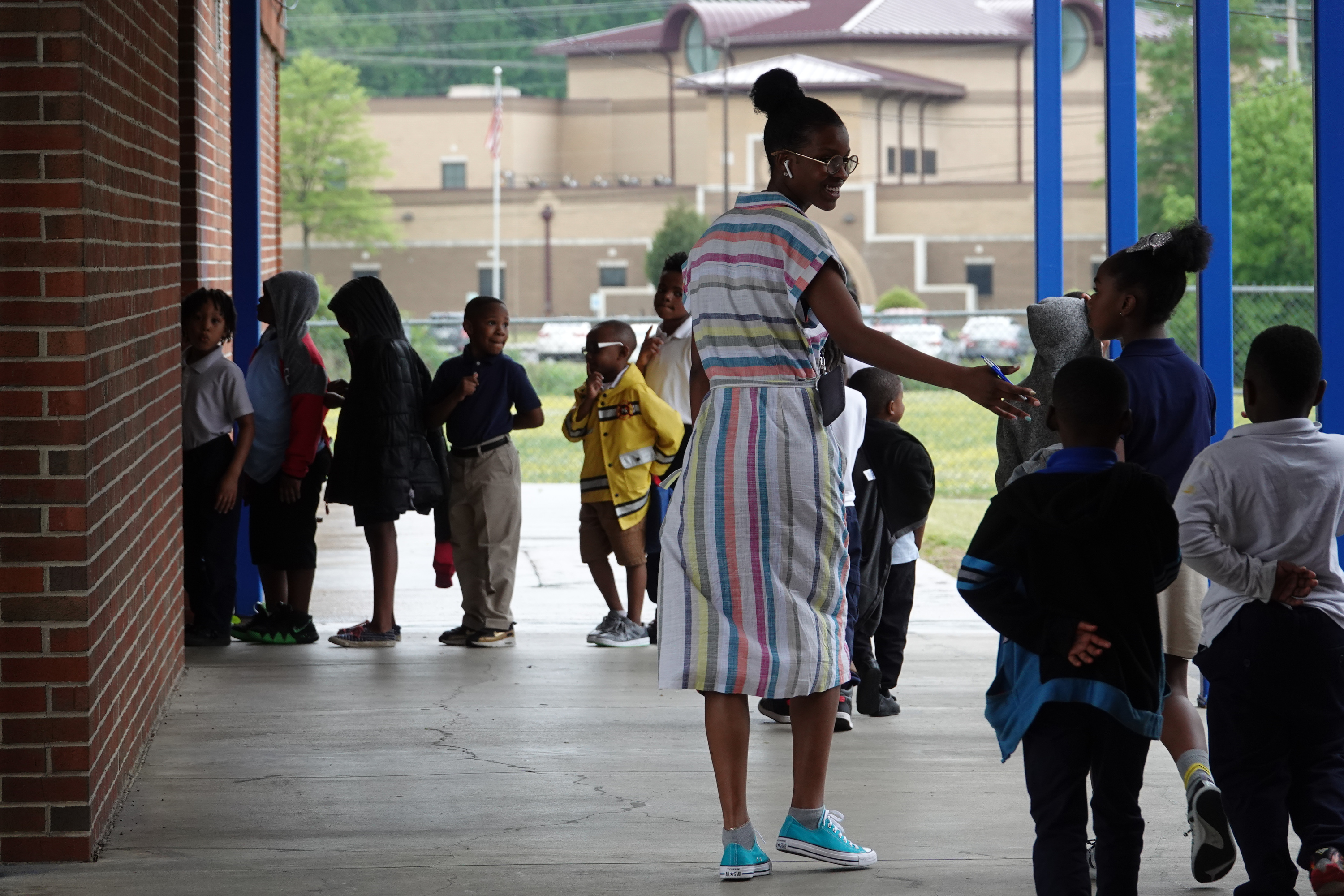 An elementary teacher walks with her student to another classroom outside.