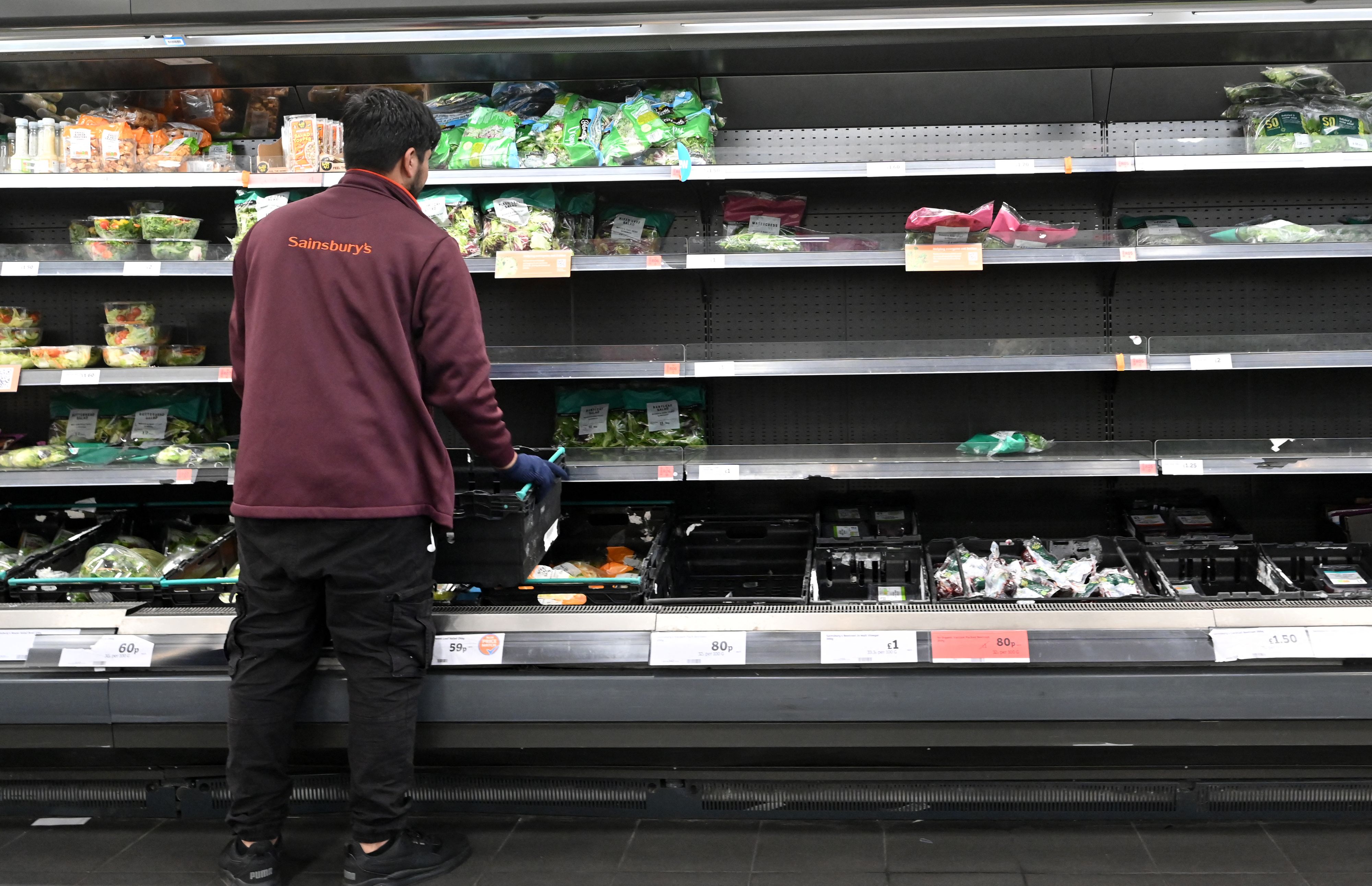 Empty fresh produce shelves at Sainsbury’s are tended to by a staff member
