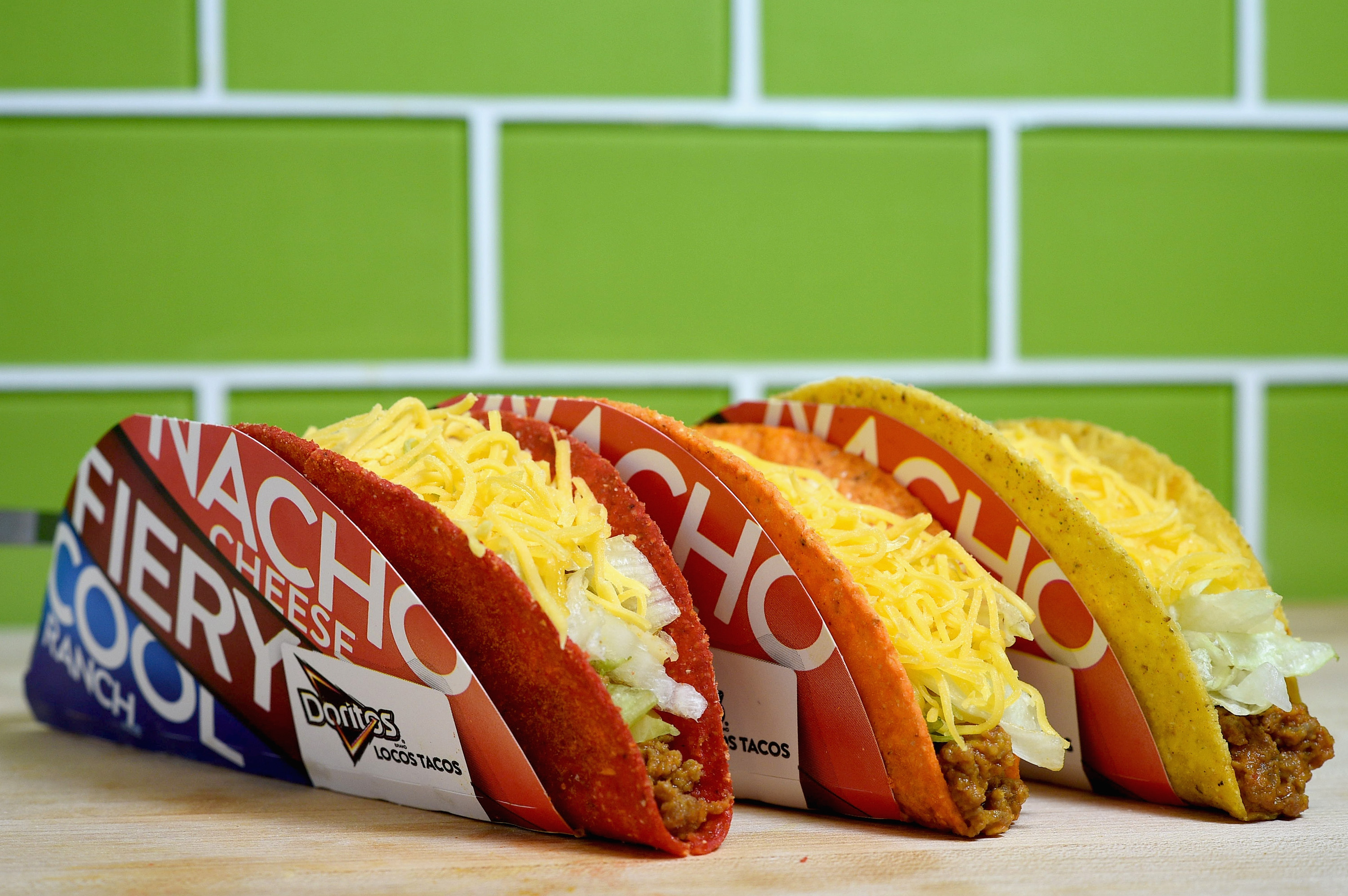 Three Taco Bell Doritos Locos Tacos in front of a green tile wall