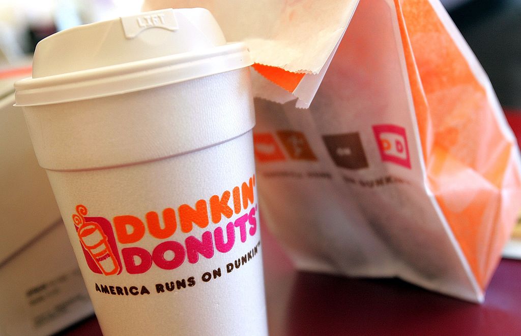 A cup of Dunkin’ Donuts coffee and a donut bag sit on a counter 