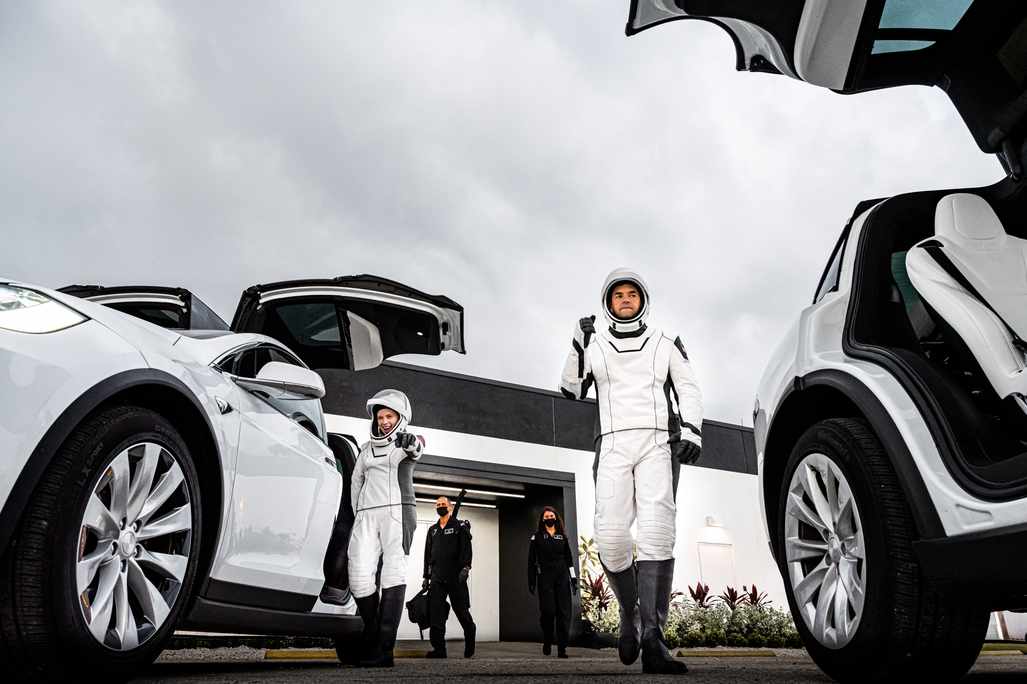 People in astronaut suits exit cars with gull-wing doors.