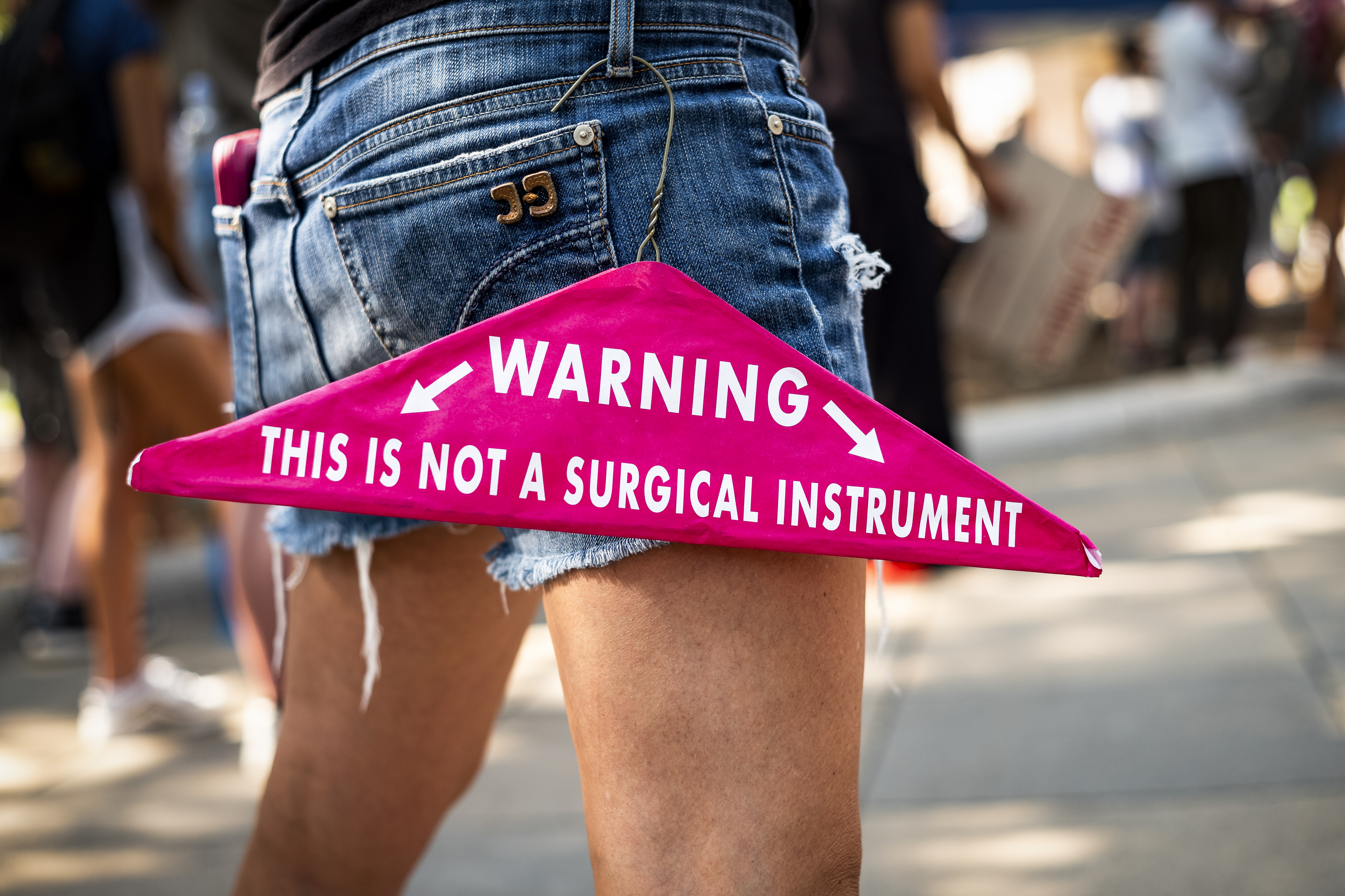 A wire hanger hooked on a person’s belt loop reads, “Warning, this is not a surgical instrument.”