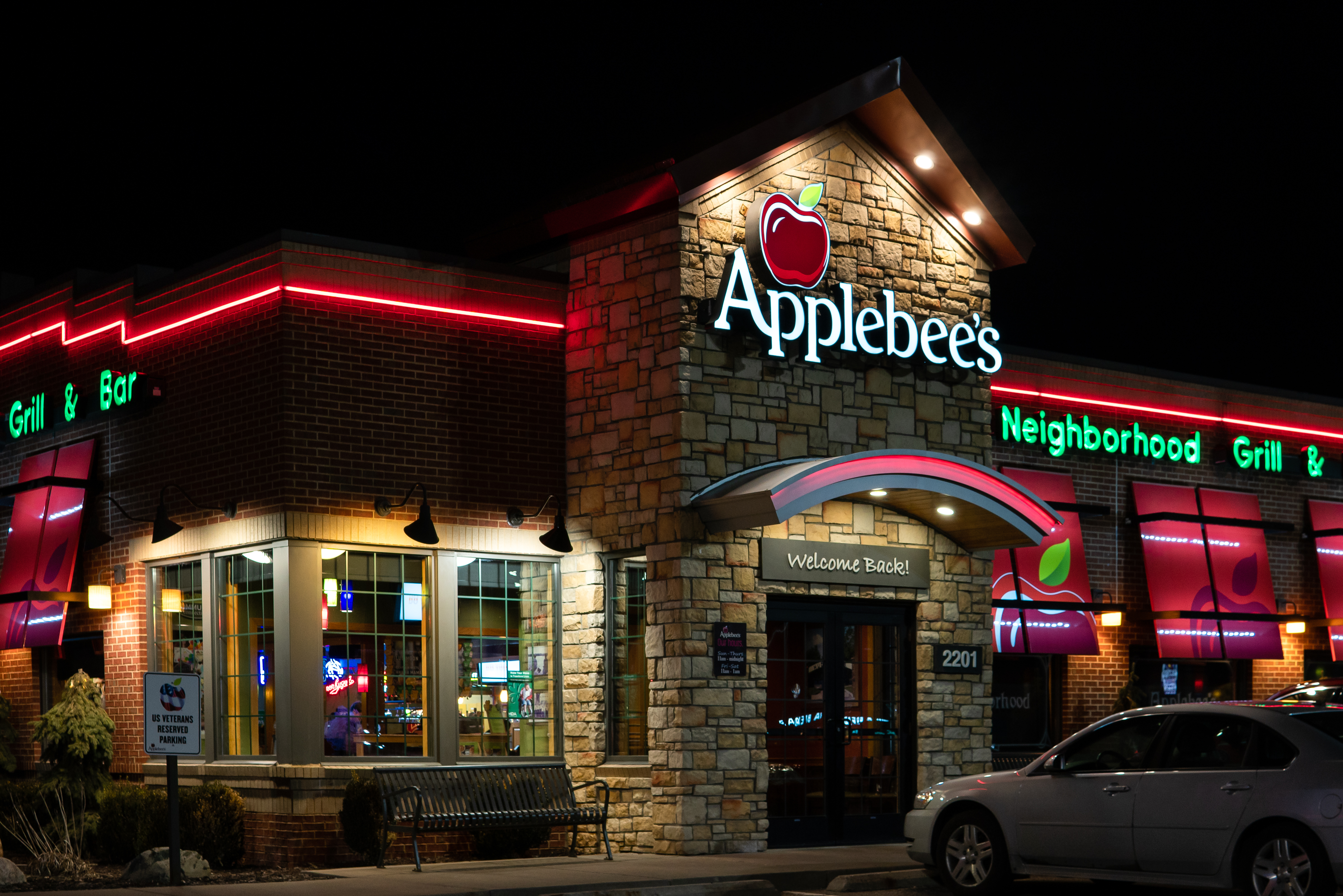 At night, the beige brick exterior of an Applebee’s restaurant is illuminated by red and green neon lights