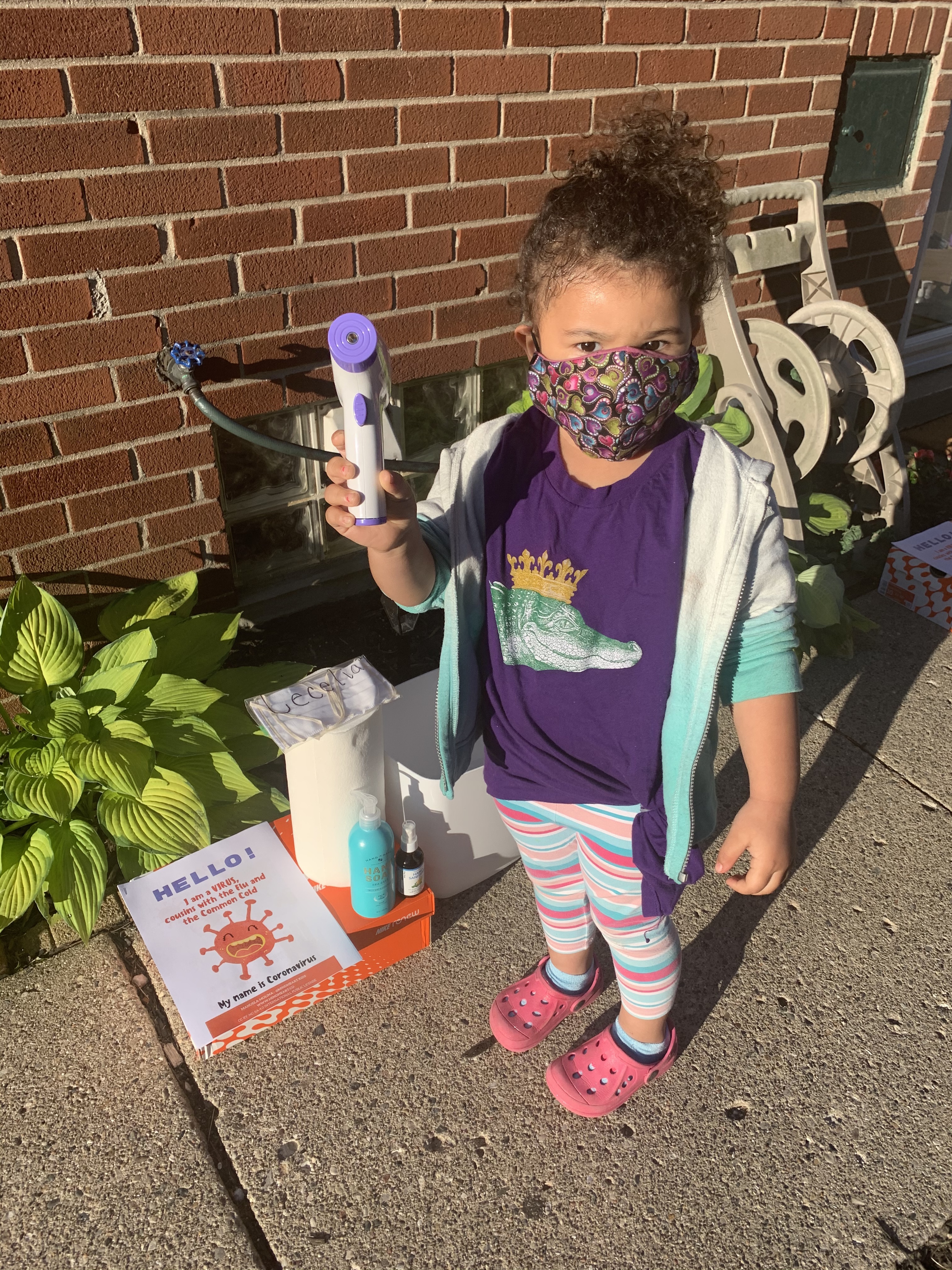 child in purple shirt stands with mask and thermometer outside of child care center in Detroit