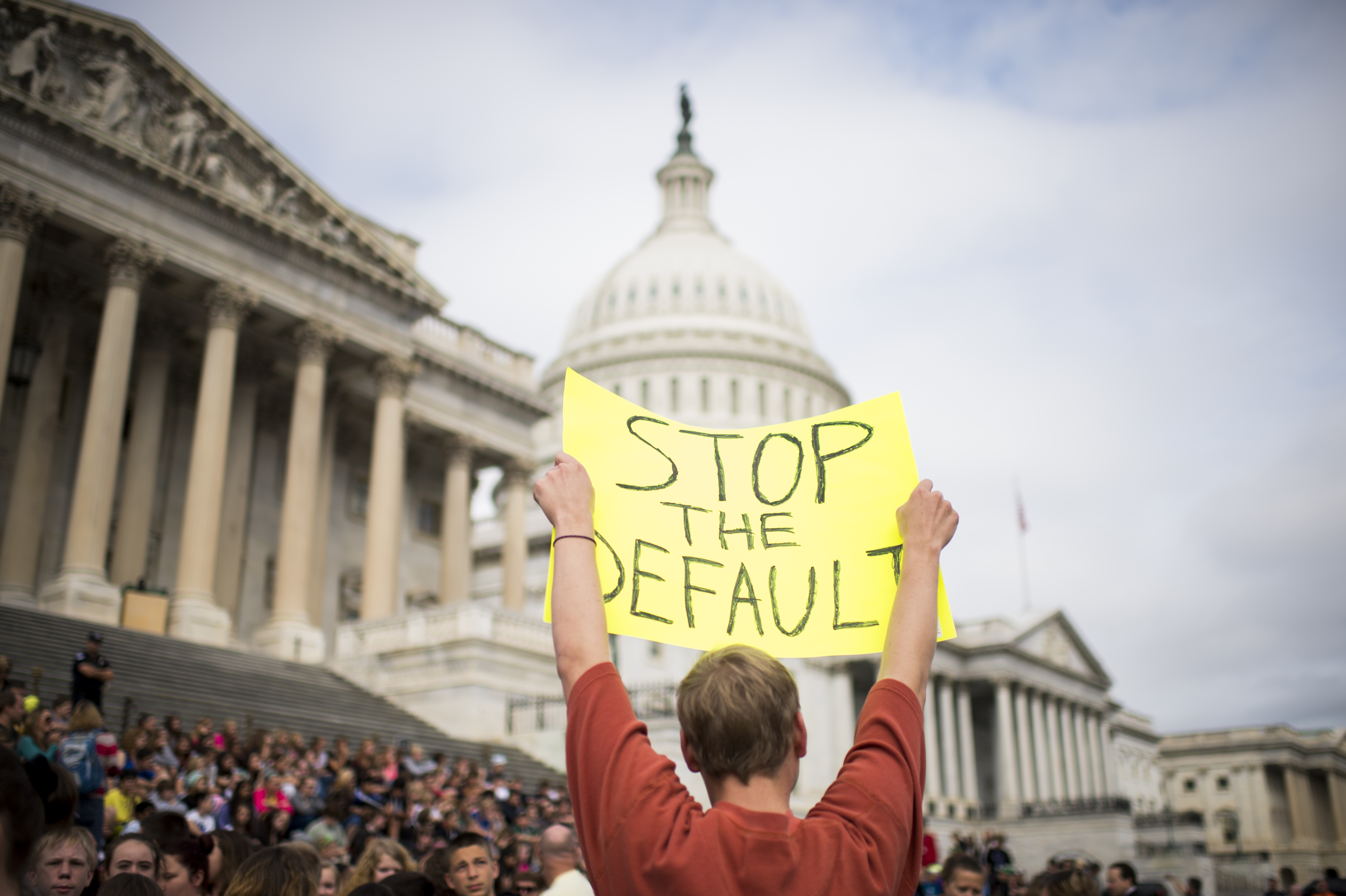 A protester holds up a sign that reads, “Stop the default” in front of the US Capitol building.