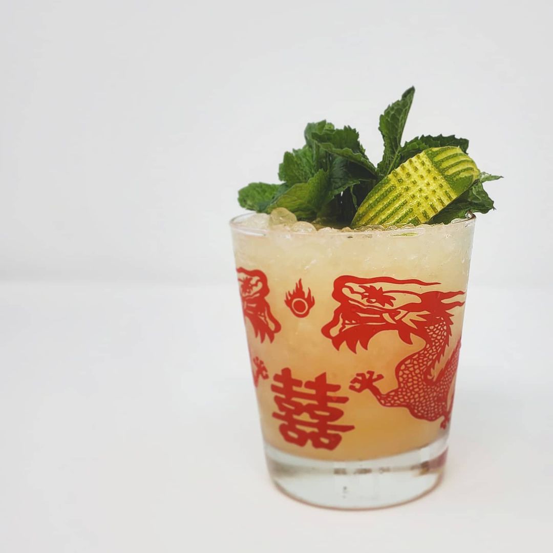 Isolated on a white background, a mai tai is in a glass decorated with a red Chinese-style dragon. The drink is garnished with a lime —&nbsp;decorative slices made into its skin —&nbsp;and fresh mint leaves.