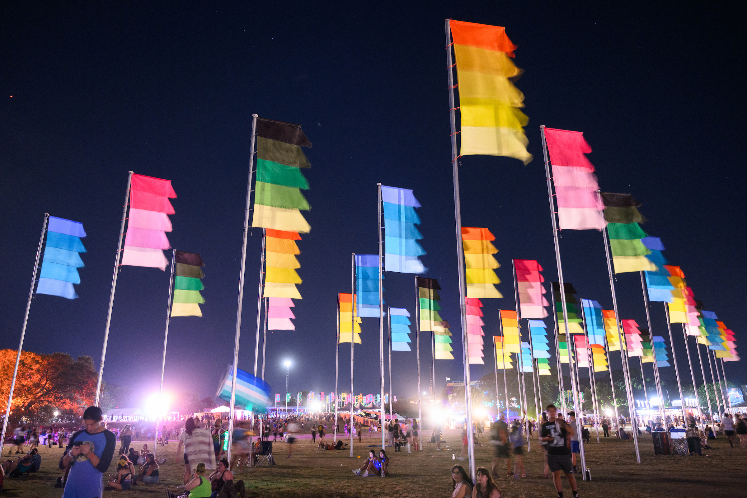 A festival grounds at night with tall colorful flags.