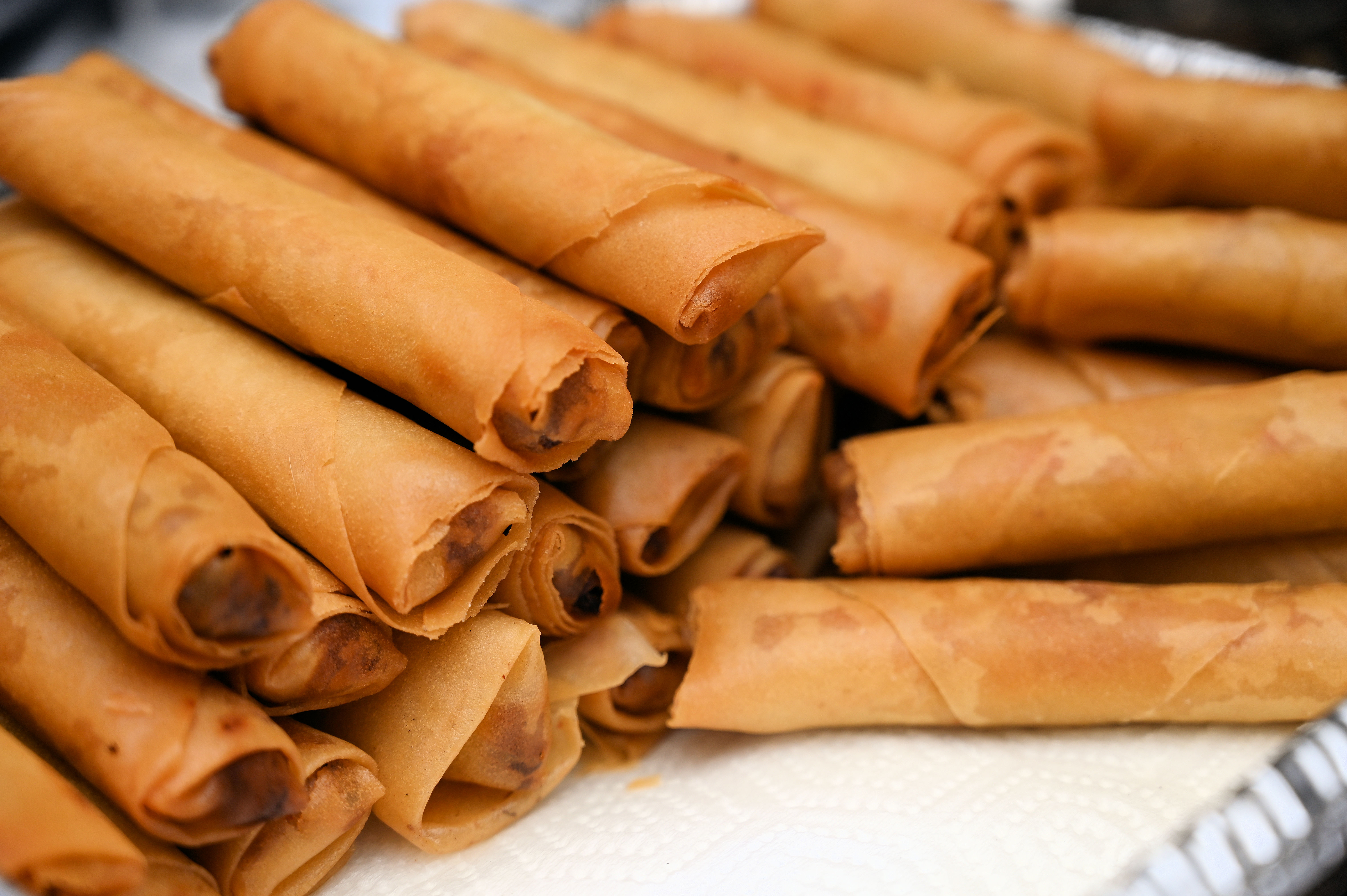 A stock photo of a plate stacked with rows of crispy lumpia. 