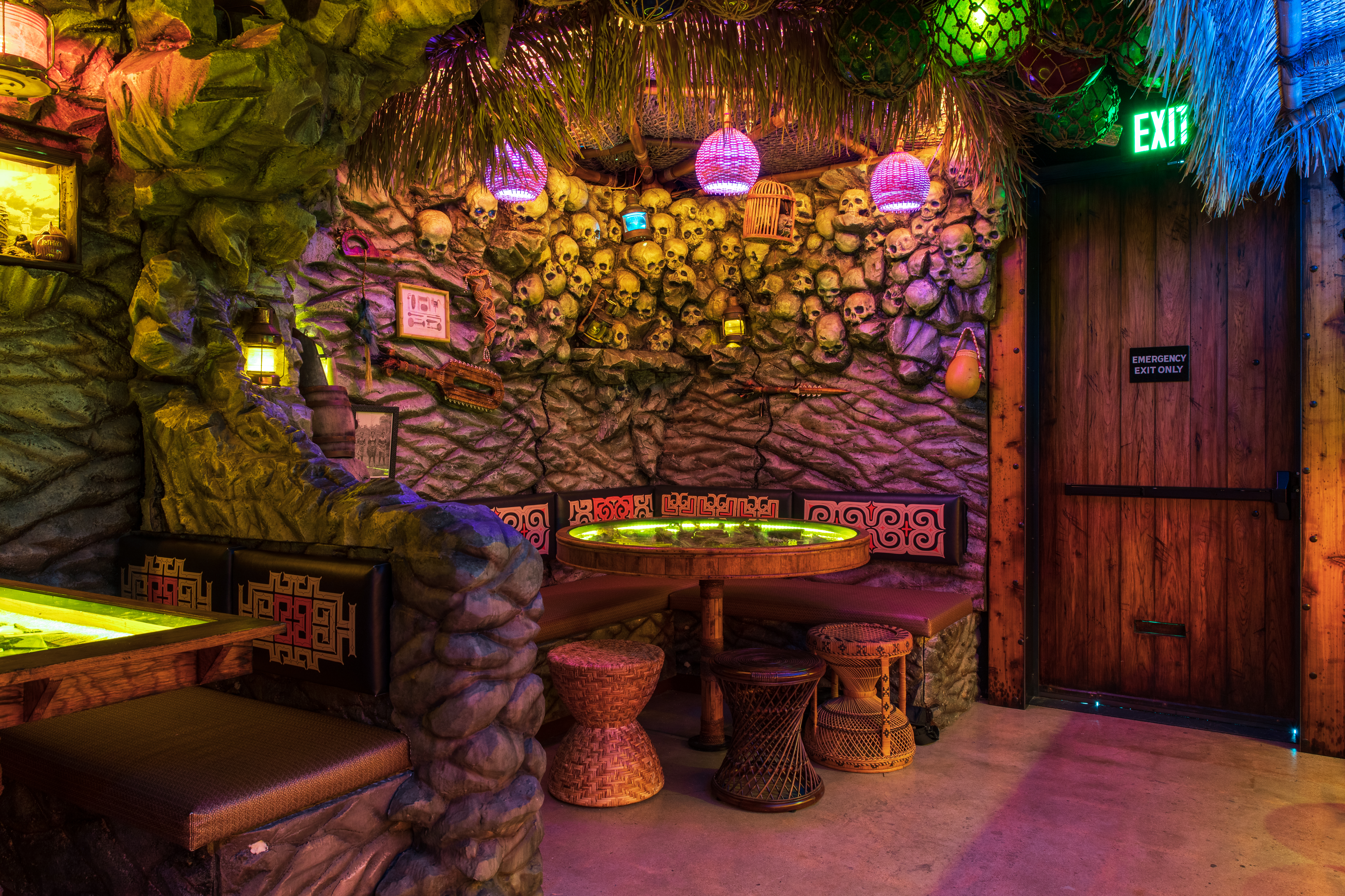 Under colorful lamps, fronds, and netting, a corner booth is nestled into a rock wall inlaid with skulls.