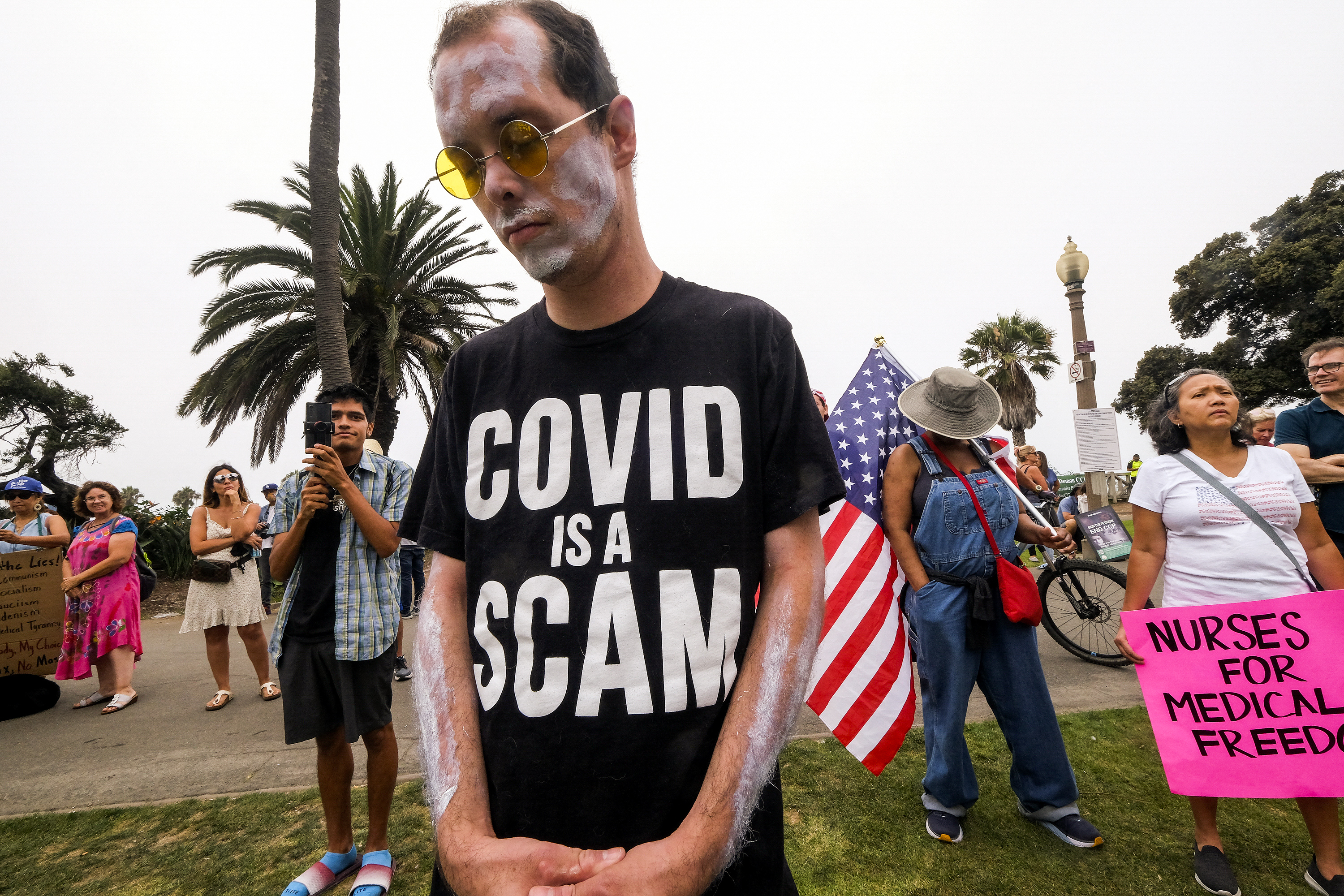 A person wearing a T-shirt that reads, “Covid is a scam.”