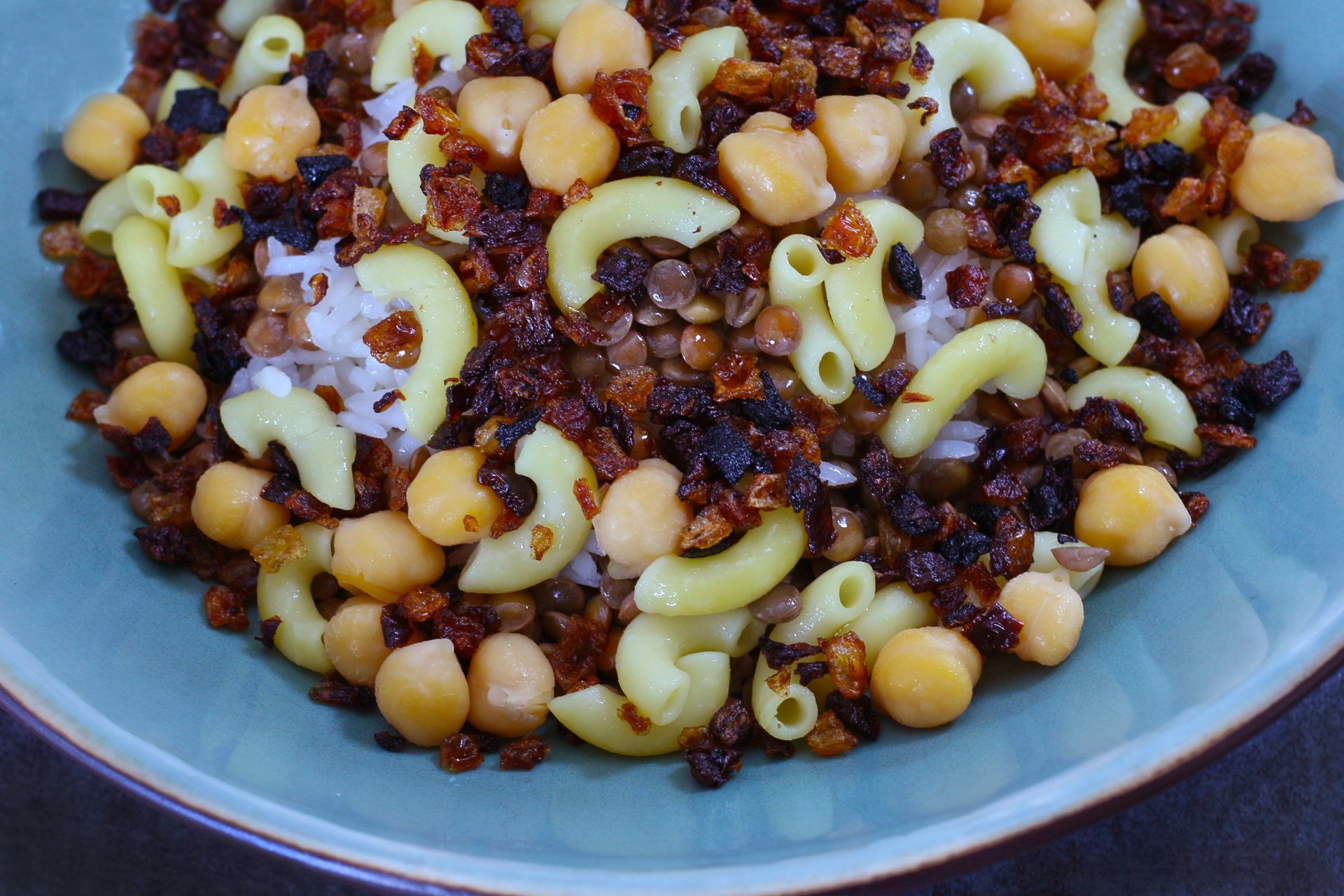 A blue bowl filled with koshari, an Egyptian dish of red lentils, macaroni noodles, chickpeas, and rice