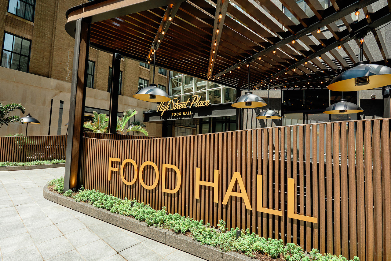 A fence made of dark wooden slats has orange lettering on it that reads food hall in capital letters.